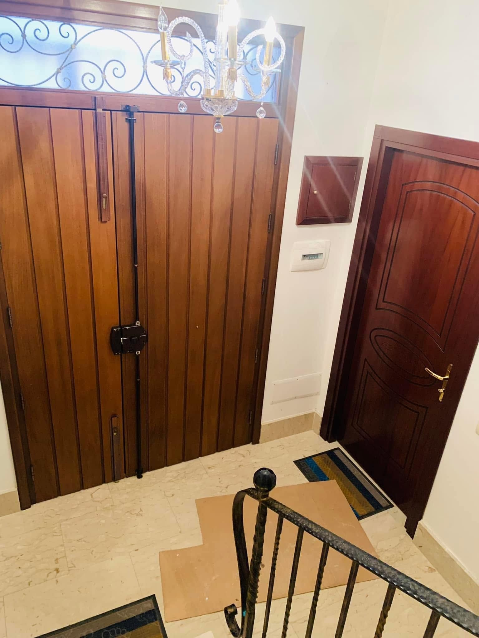 Pianerottolo interno delle scale con cancelli in legno, porta scura e pavimento in piastrelle color crema.