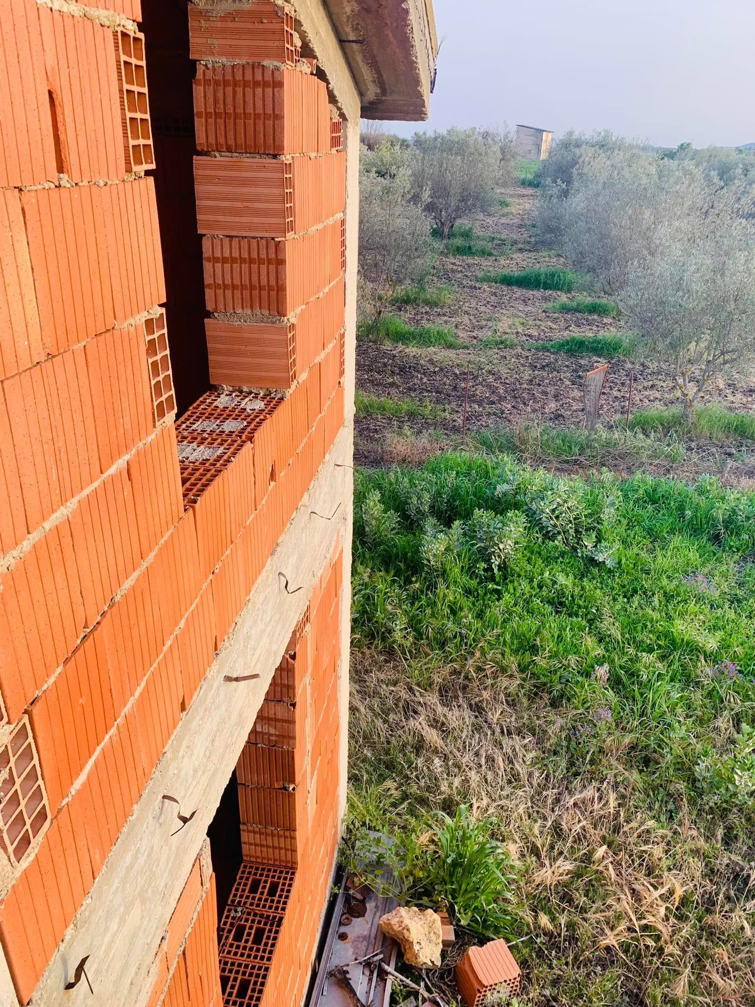Muro di mattoni parzialmente costruito con apertura per finestra accanto a un campo erboso, illuminato dal giorno.
