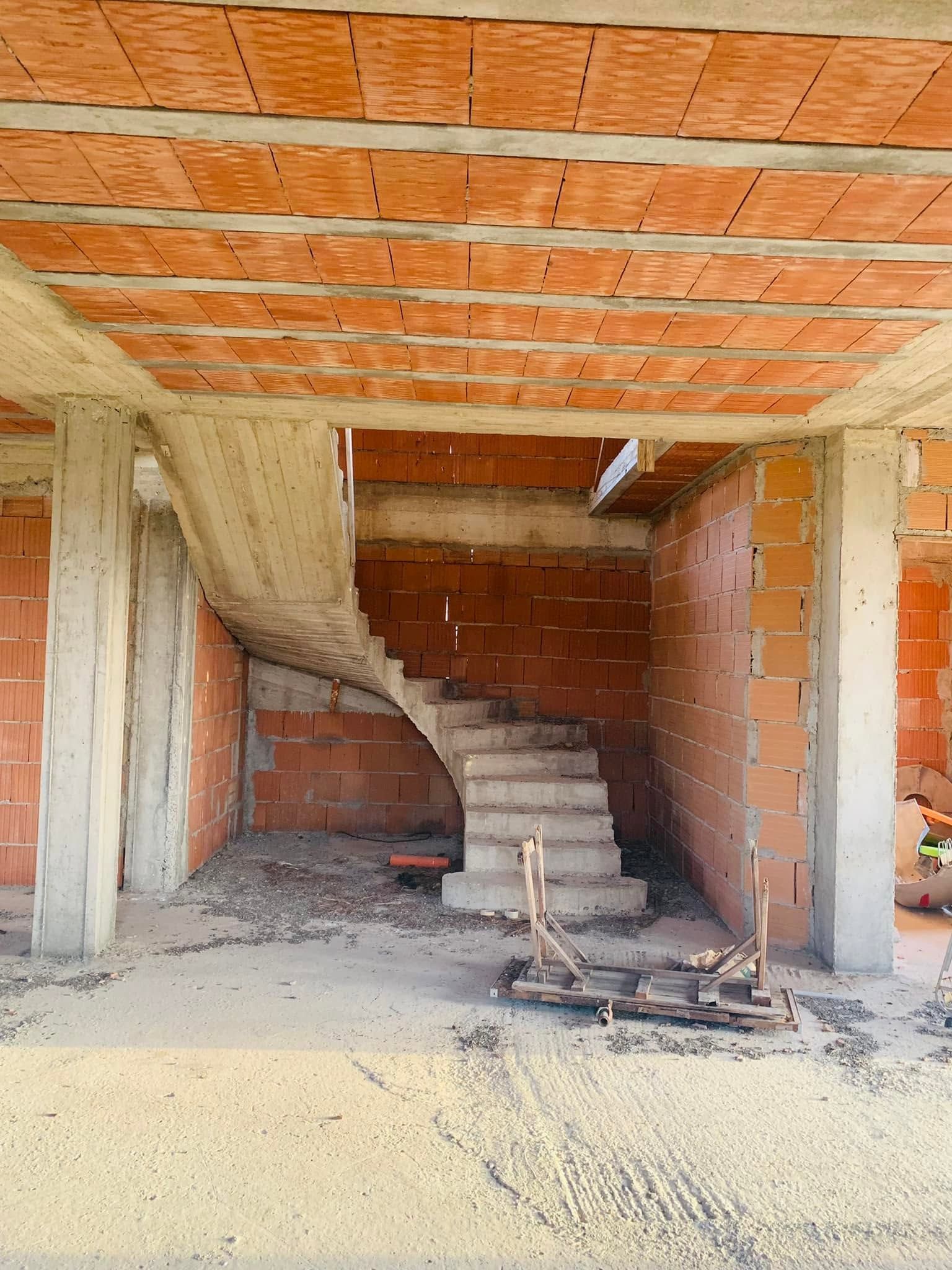 Interno di una casa in cemento grezzo con scala in mattoni e pareti in mattoni rossi a vista.