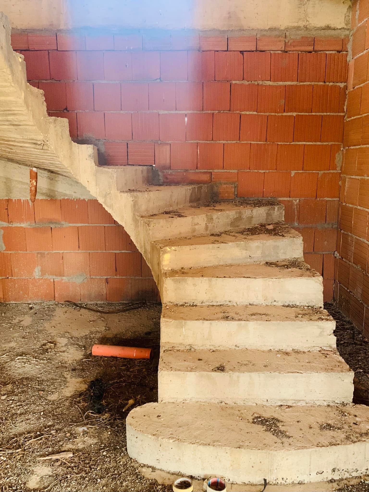 Scala curva in cemento all'interno di una parete in mattoni a vista, con un piccolo lucernario soprastante.