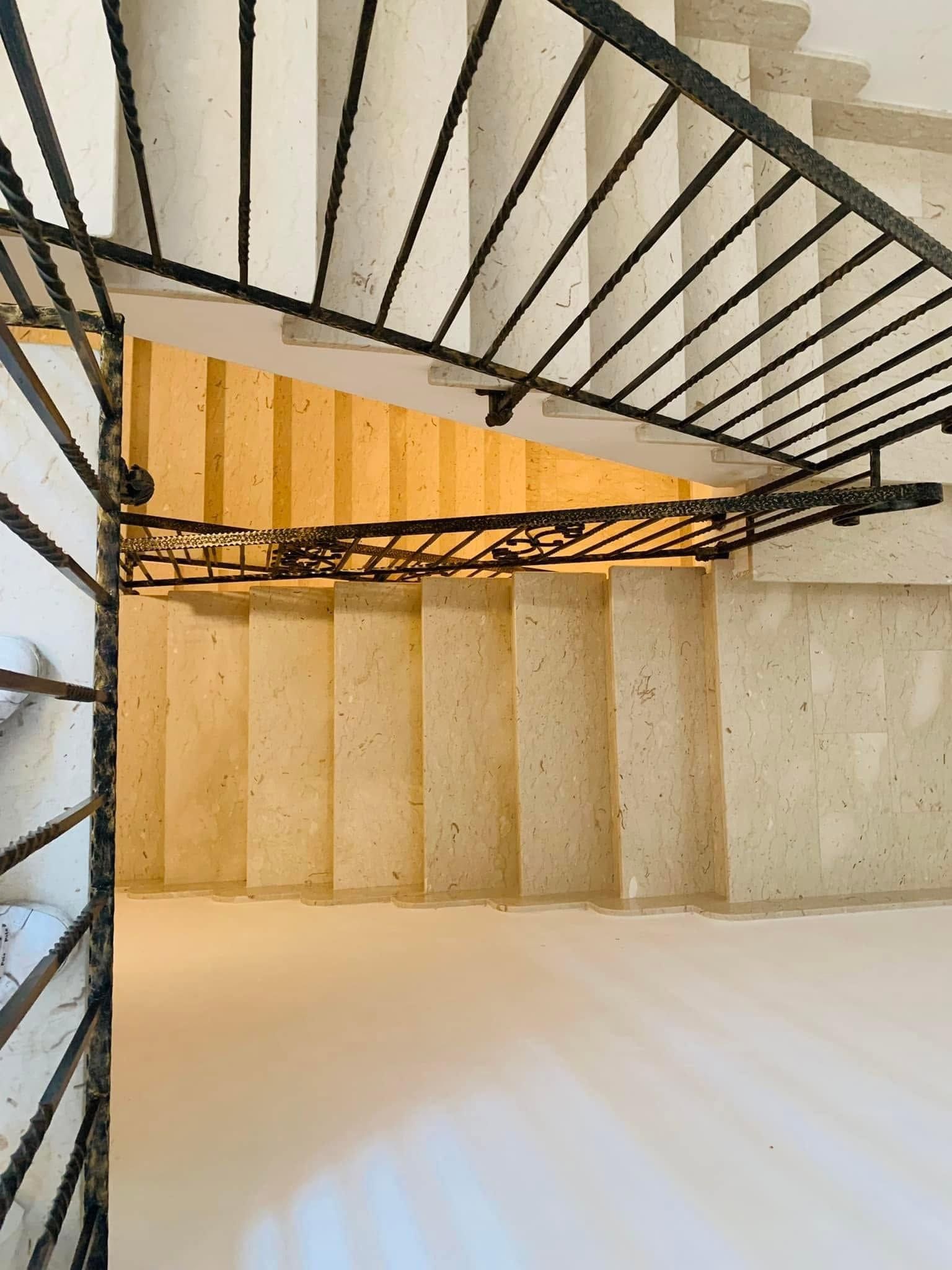 Vista dall'alto di una scala a chiocciola con ringhiere nere e gradini beige in un interno moderno.