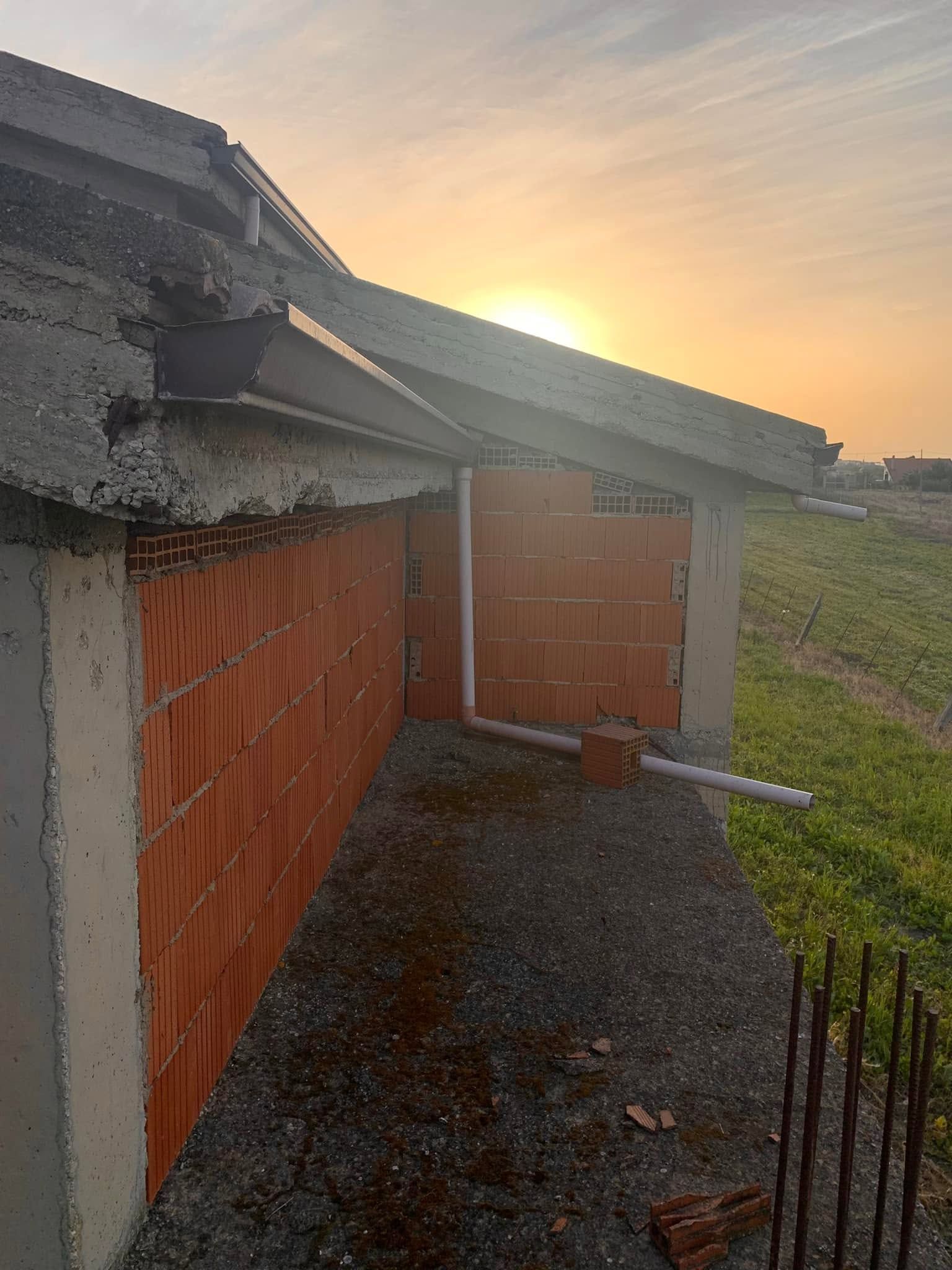 Sentiero di ghiaia accanto a un edificio in mattoni al tramonto, con il tetto danneggiato e un cancello di metallo.