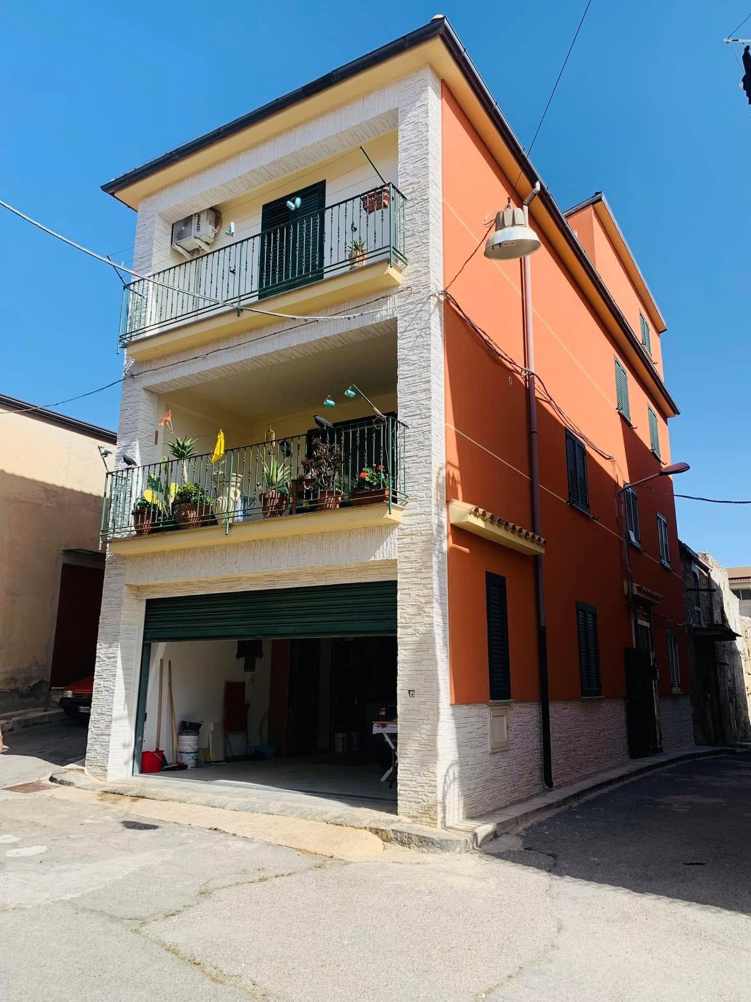 Edificio residenziale angolare di tre piani con balconi, facciata arancione e bianca, situato in una strada soleggiata.