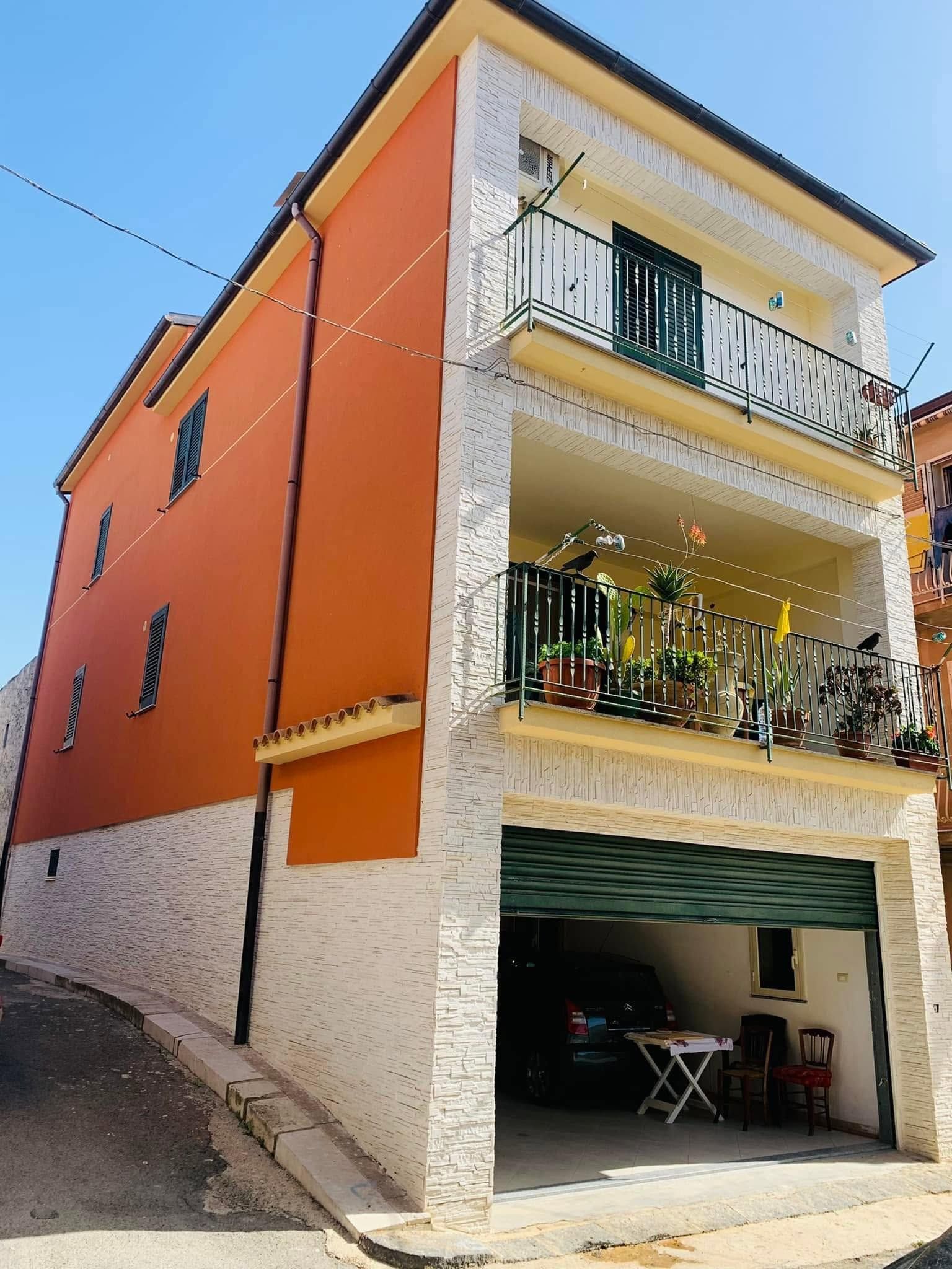 Palazzo di appartamenti color arancione brillante con balconi e garage, situato su una strada in salita.