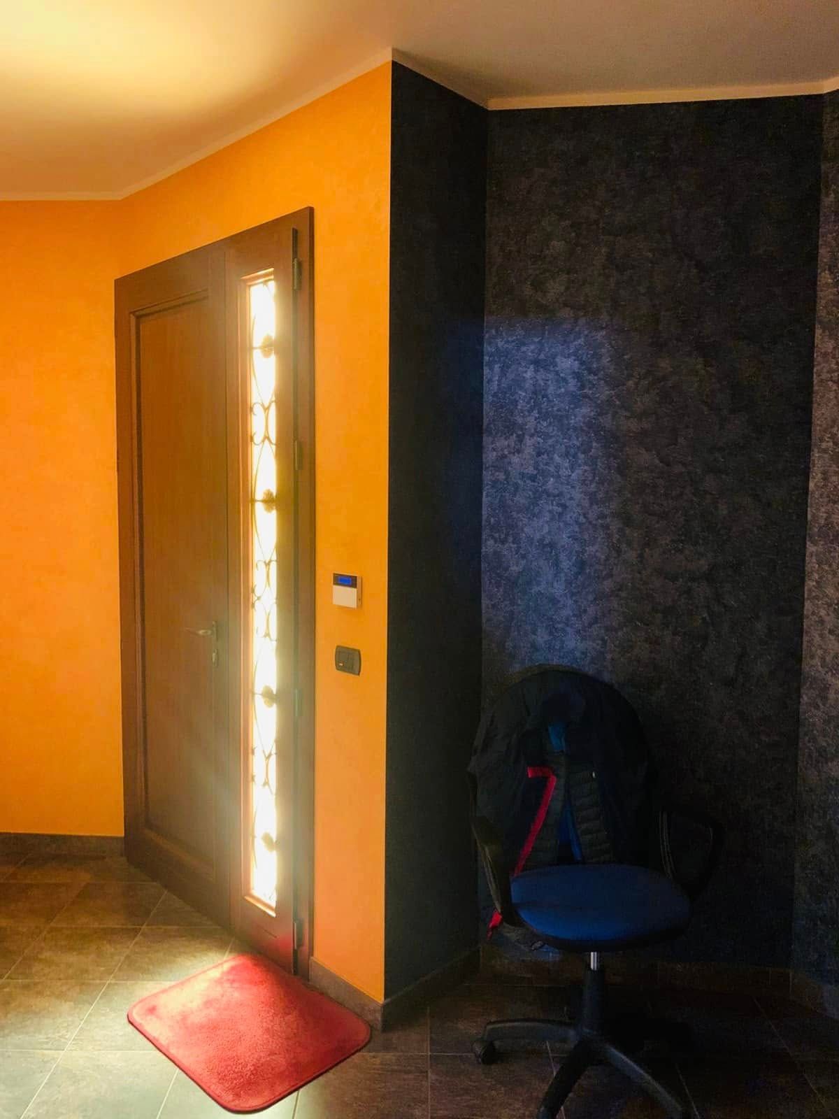 Porta d'ingresso in un corridoio arancione con uno zerbino rosso e una sedia nera in una nicchia buia