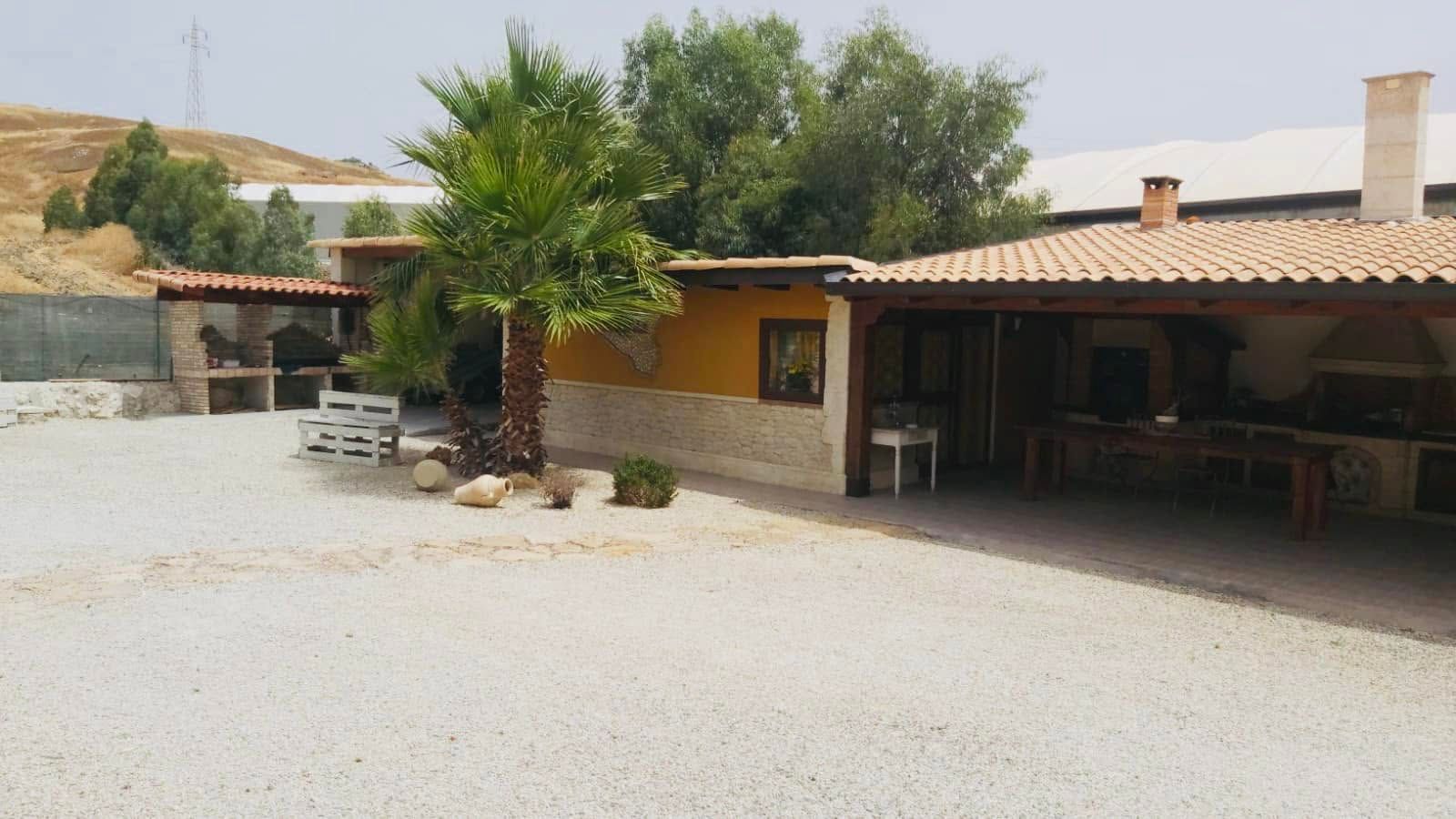 Casa rurale in pietra con un ampio cortile ghiaioso, alberi e un portico ombreggiato con tetto di tegole.