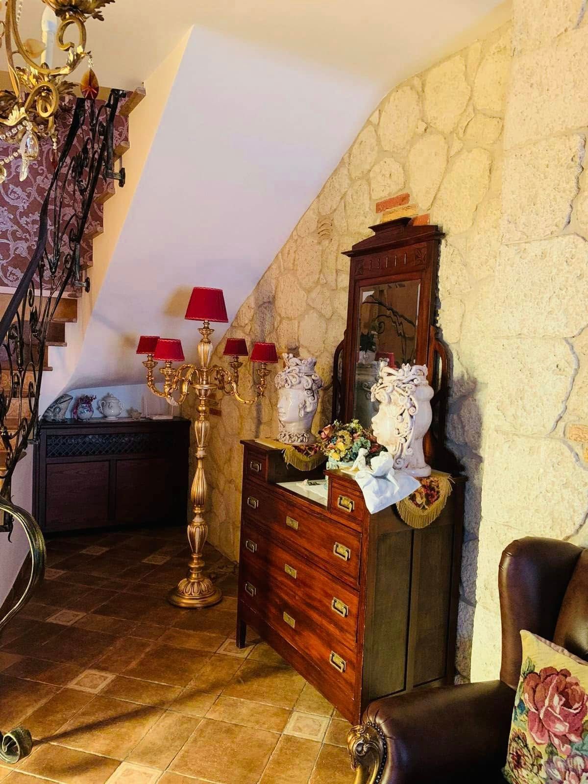 Elegante corridoio con cassettiera antica in legno, lampada dorata, paralumi rossi e parete con finitura effetto pietra.