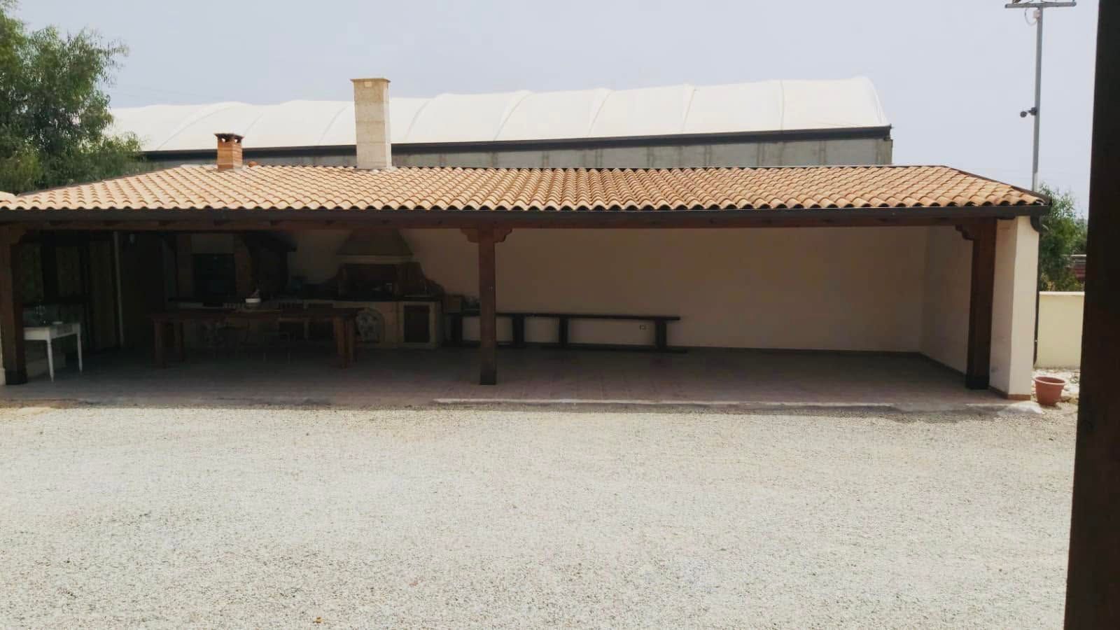 Casa a un solo piano con tetto in tegole e patio ombreggiato in un cortile ghiaioso.