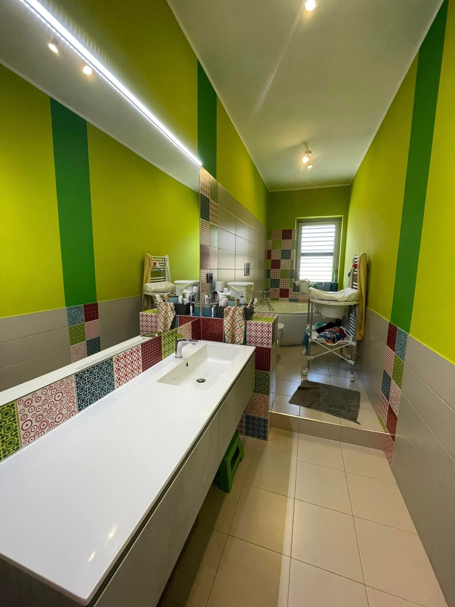 Bagno a strisce verde brillante con lavandini, pavimento piastrellato e un lungo bancone bianco all'interno di una stanza stretta