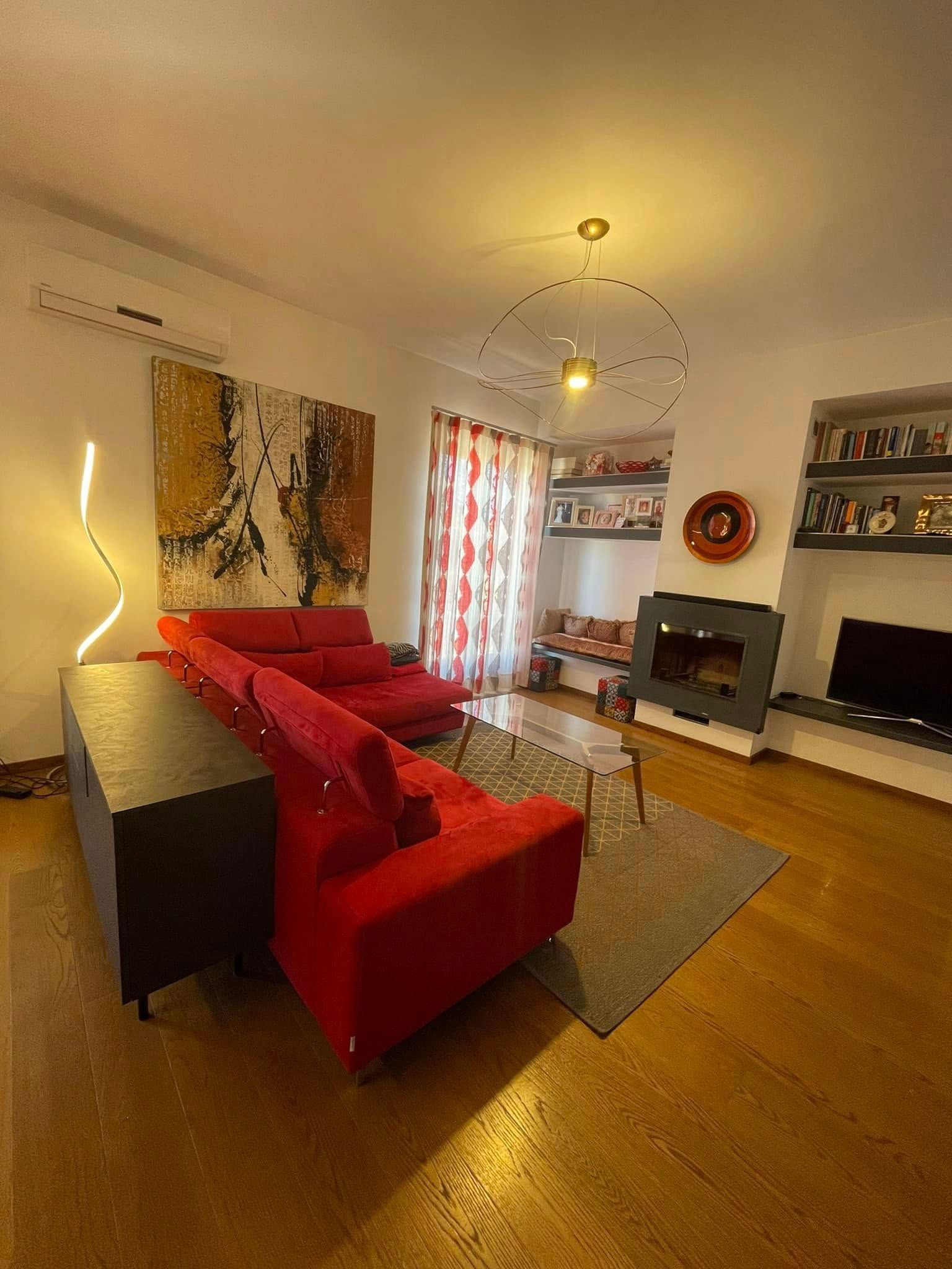 Soggiorno moderno con divano componibile rosso, camino, TV e illuminazione calda.