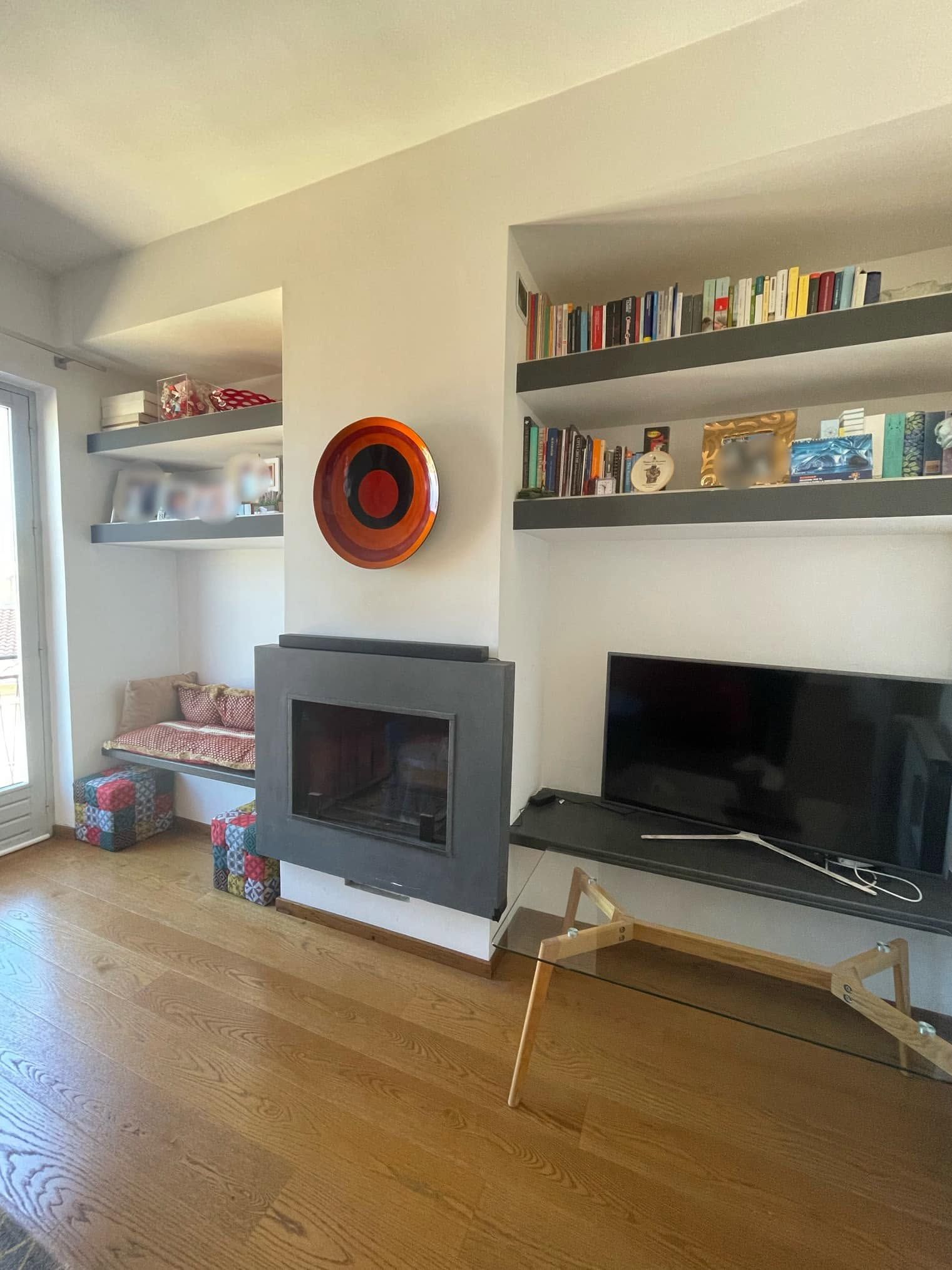 Soggiorno moderno con camino grigio, scaffali a muro, TV e pavimento in legno.