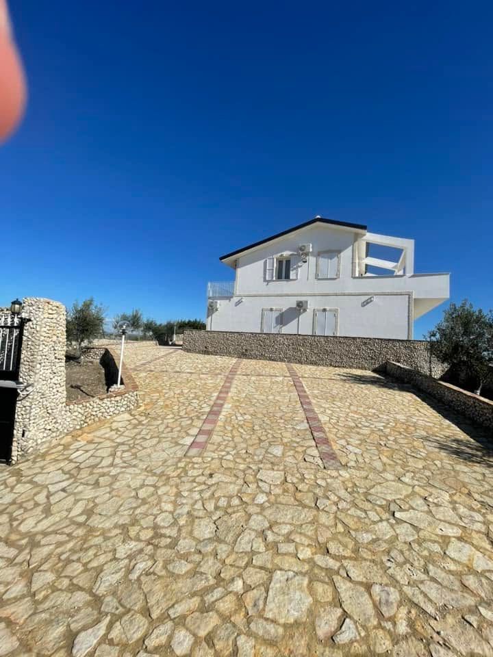 Casa bianca a due piani su un vialetto di pietra sotto un cielo azzurro limpido