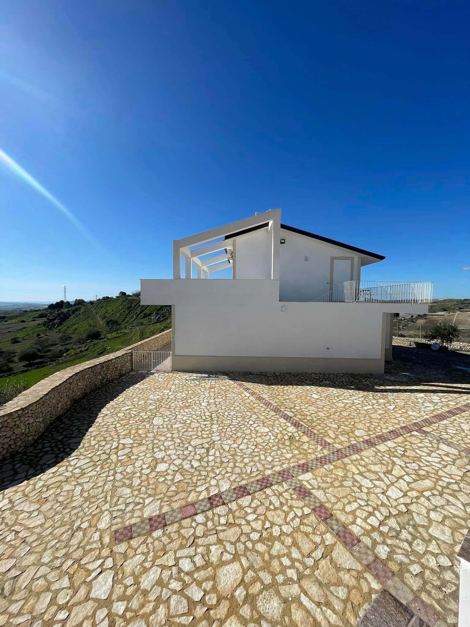 Casa moderna bianca con terrazza su un pendio lastricato in pietra sotto un cielo azzurro limpido