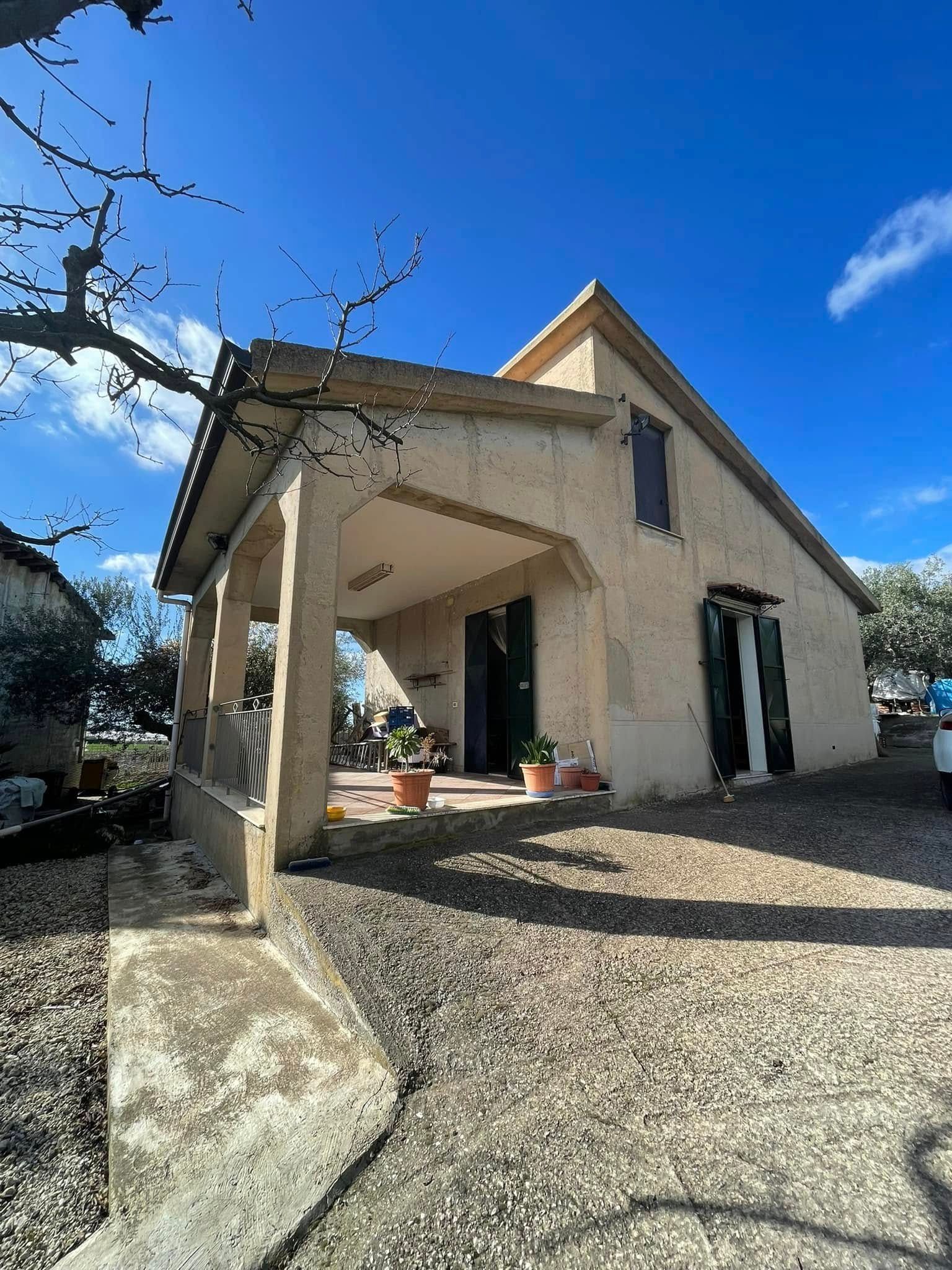 Casa beige con portico e vialetto di ghiaia sotto un cielo azzurro brillante.