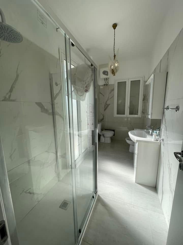Bagno moderno con doccia in vetro, mobile lavabo bianco, WC e pareti con motivo effetto marmo.