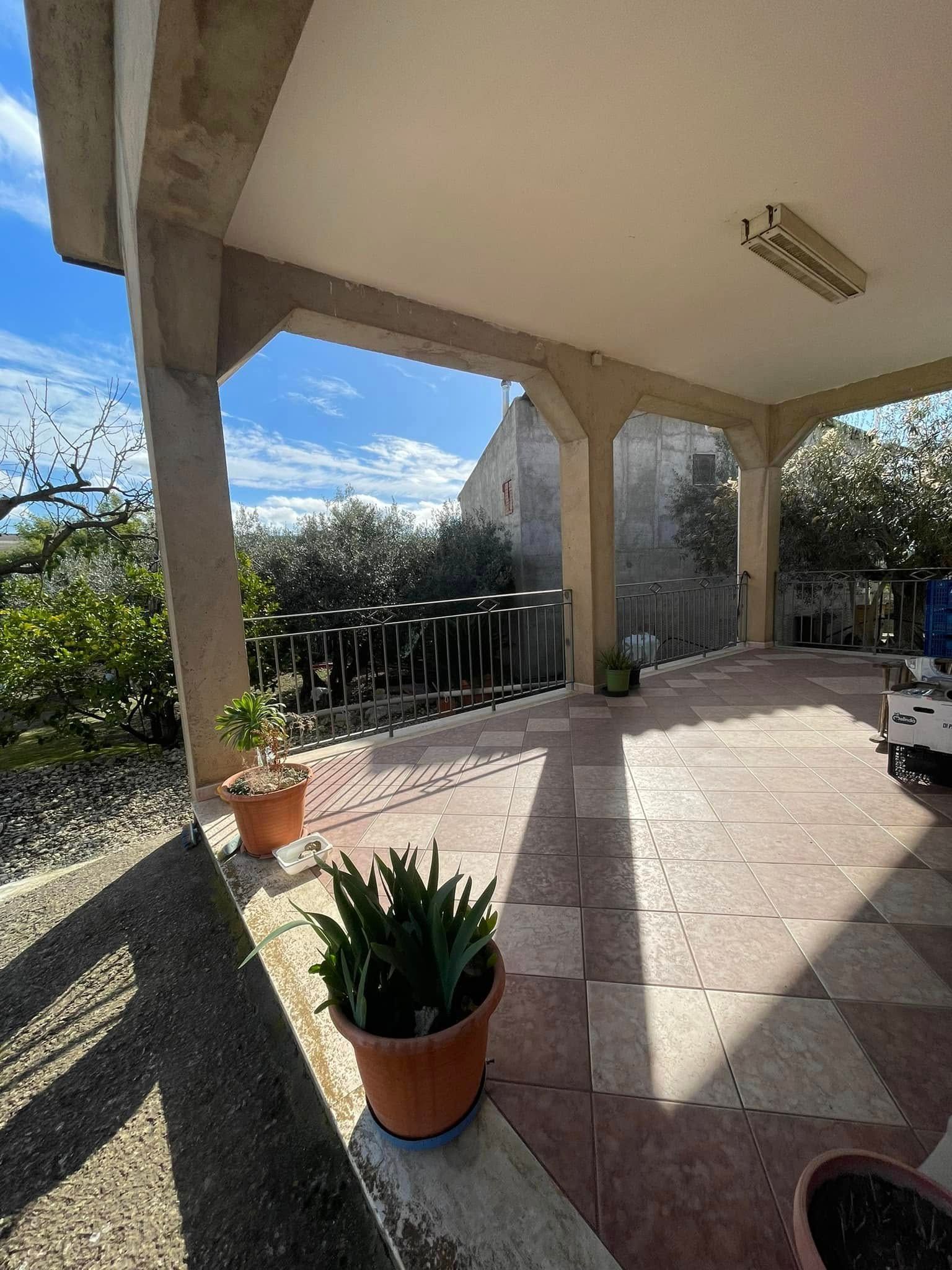 Patio piastrellato e soleggiato con piante in vaso, colonne in pietra e vista sul giardino retrostante.