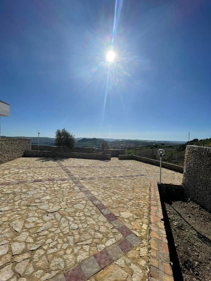 Terrazza soleggiata pavimentata in pietra con vista su un paesaggio lontano, sotto un cielo azzurro e limpido.