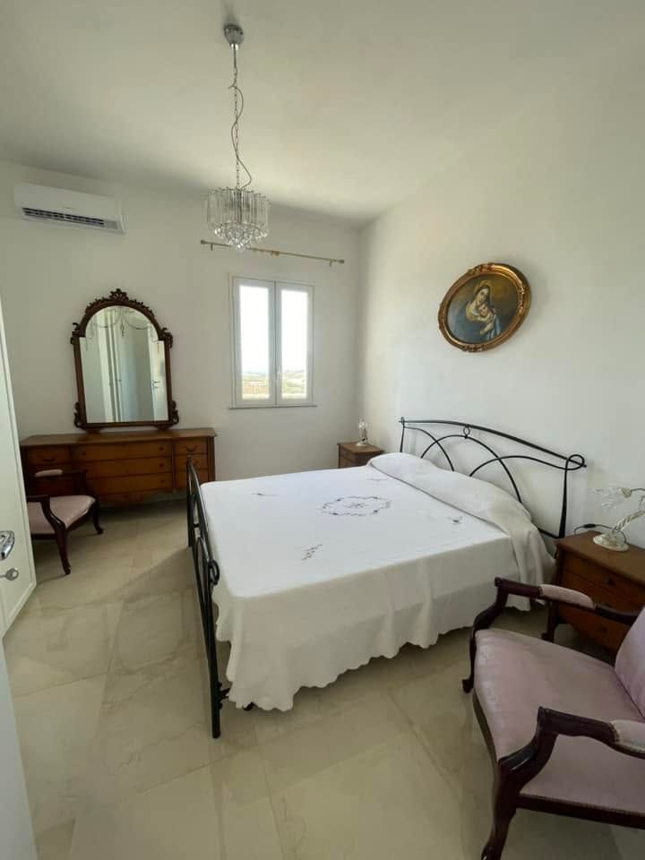 Camera da letto luminosa con letto in metallo, comò con specchio, sedia e finestra in una stanza bianca