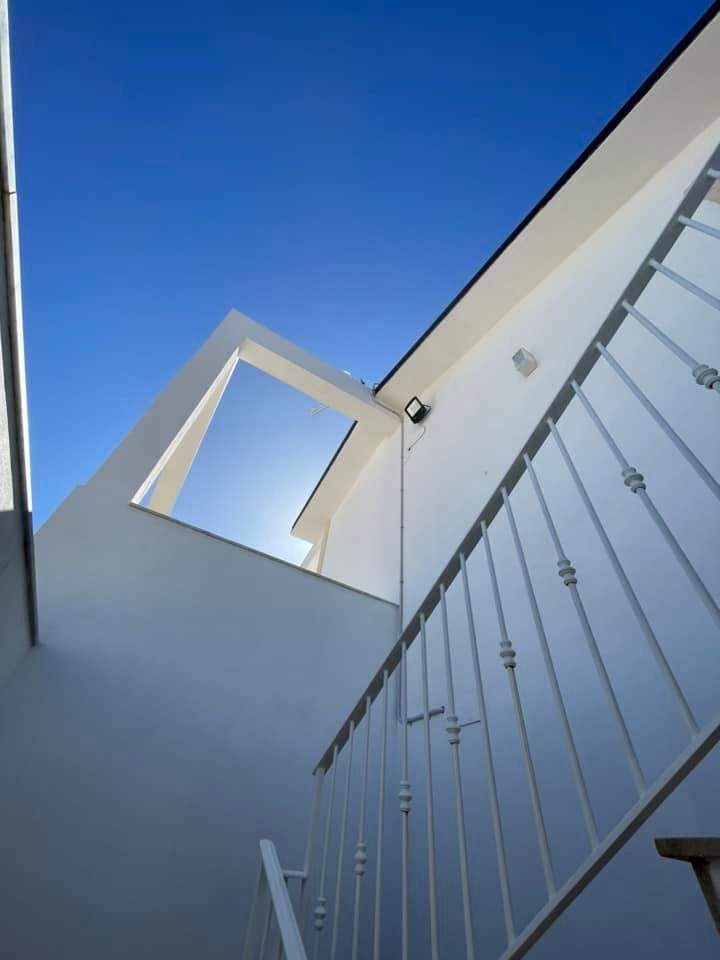 Vano scale di un moderno edificio bianco con ringhiere sullo sfondo di un cielo azzurro brillante.