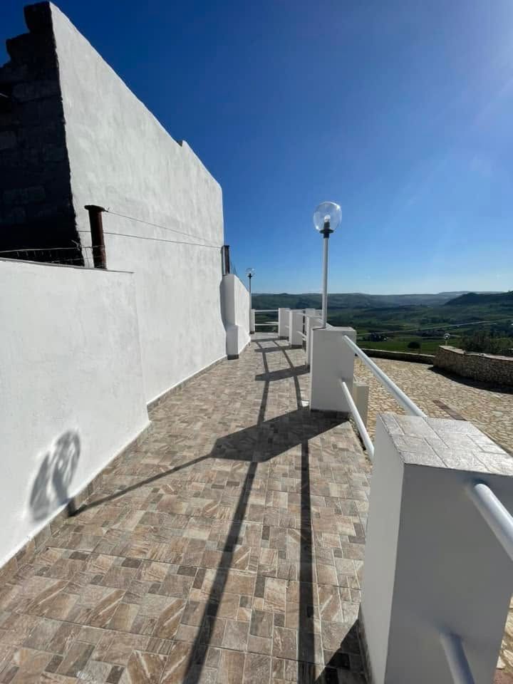 Terrazza bianca con pavimento piastrellato, lampione e vista sulle montagne sotto un cielo azzurro.