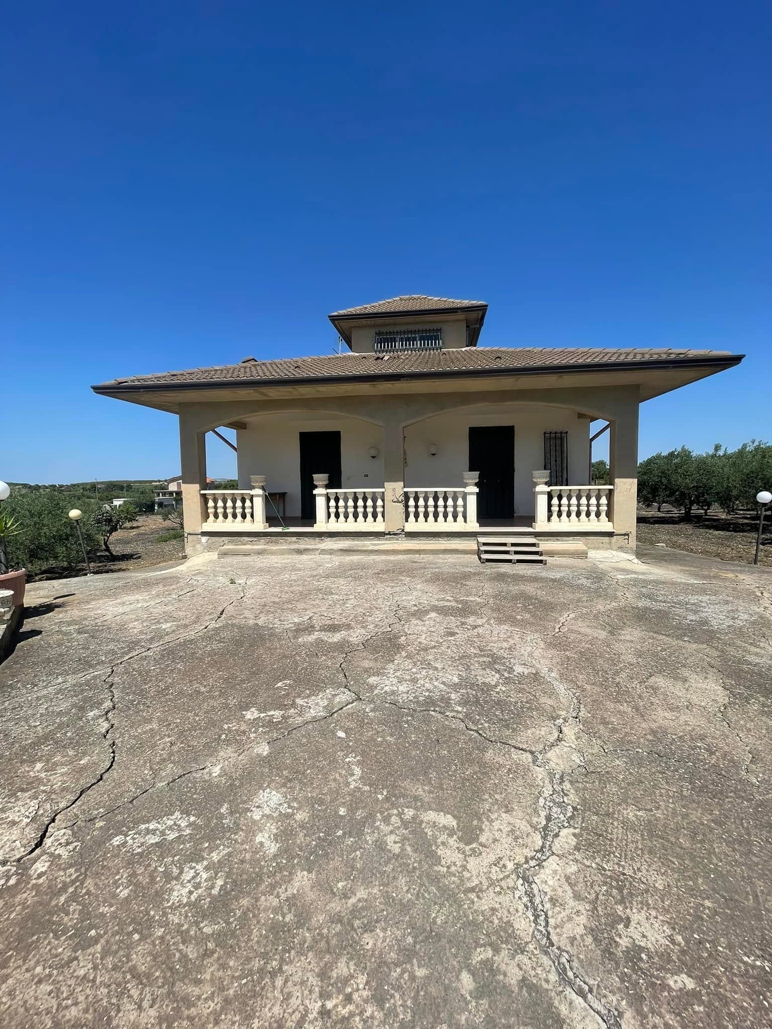 Piccola casa beige con veranda su una collina rocciosa sotto un cielo azzurro e limpido.