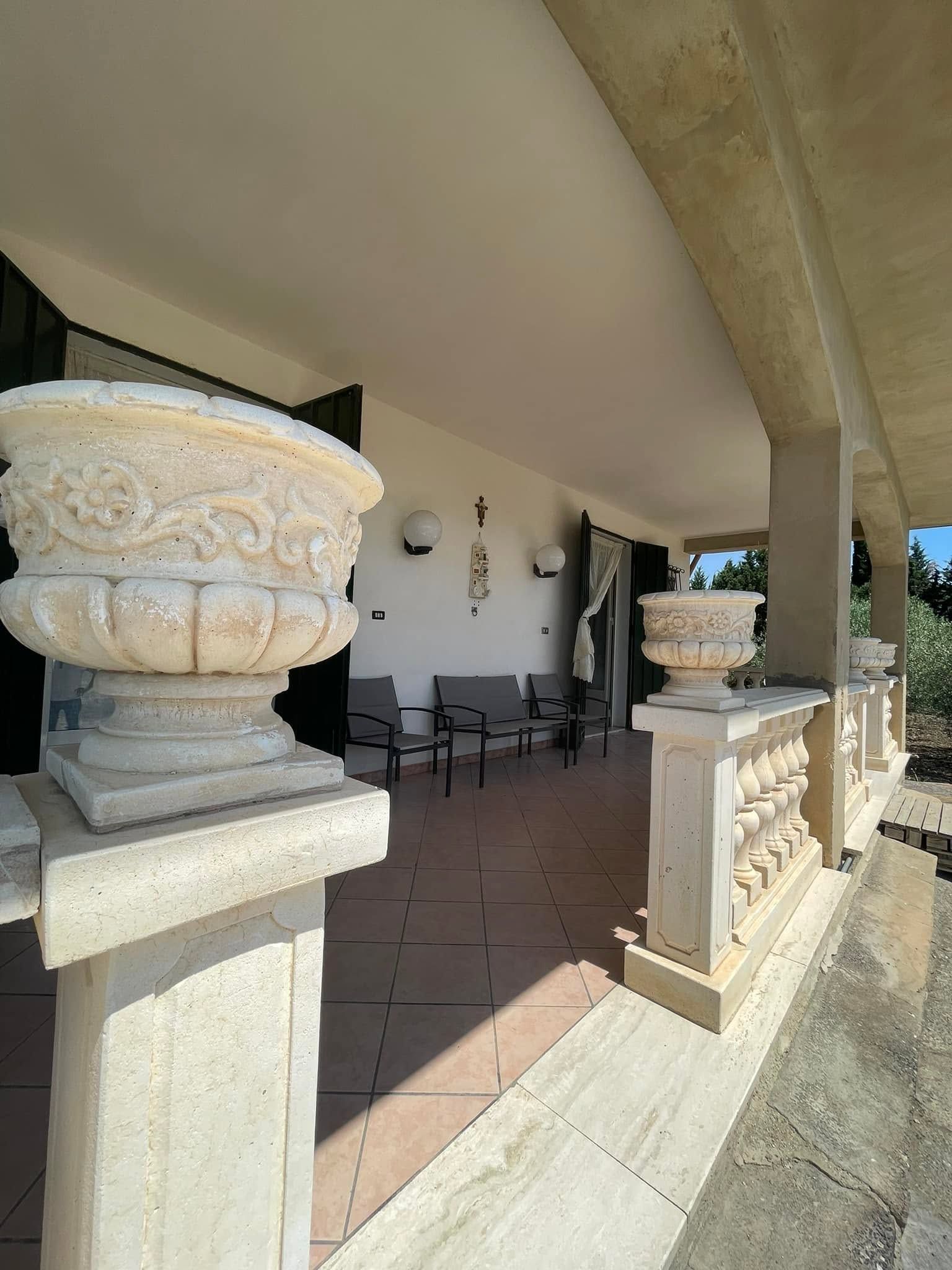 Patio coperto con fioriere bianche decorate, ringhiera e mobili da giardino all'ombra