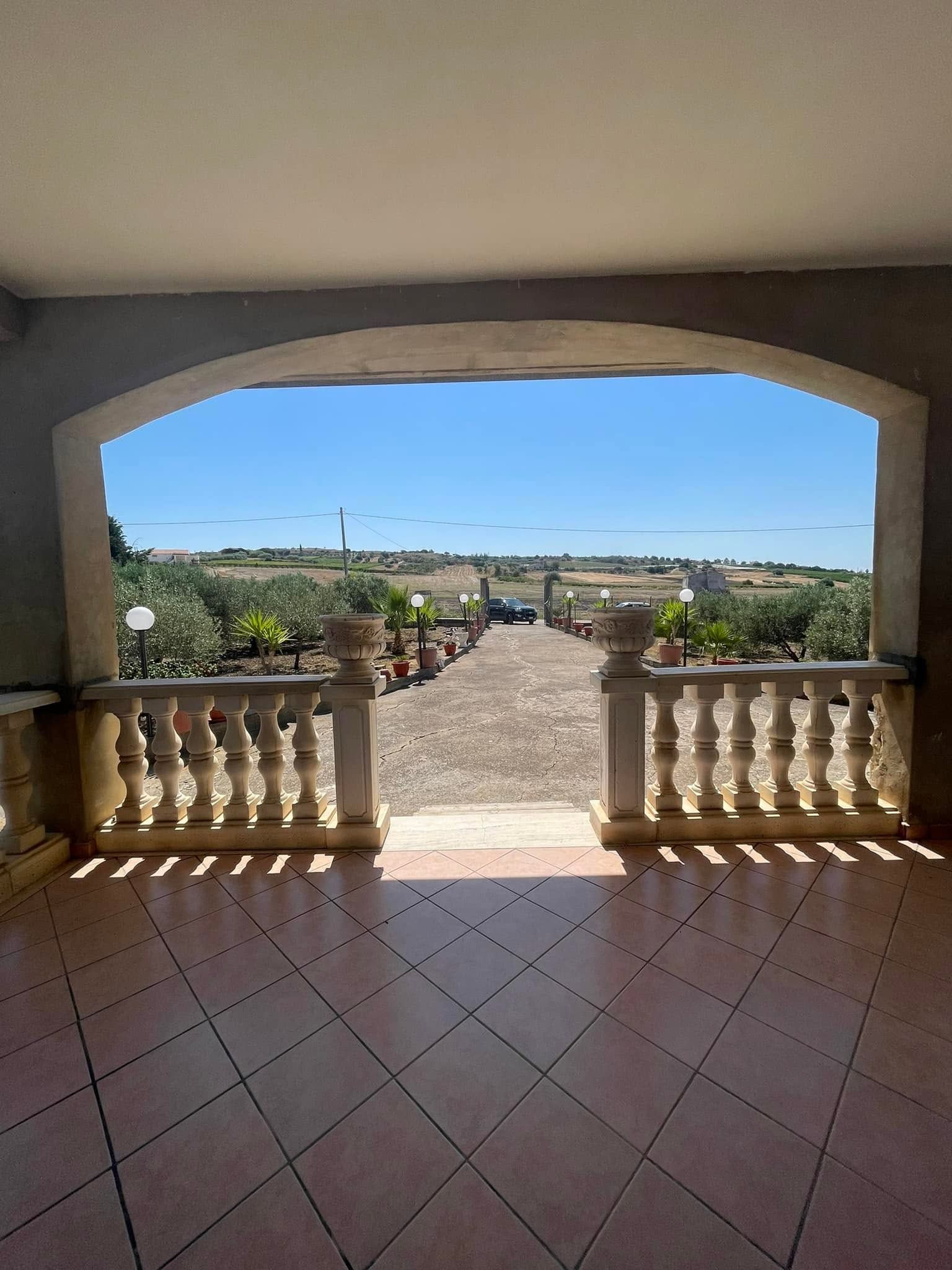 Patio con pavimento in piastrelle di terracotta e apertura ad arco che si affaccia su un giardino soleggiato
