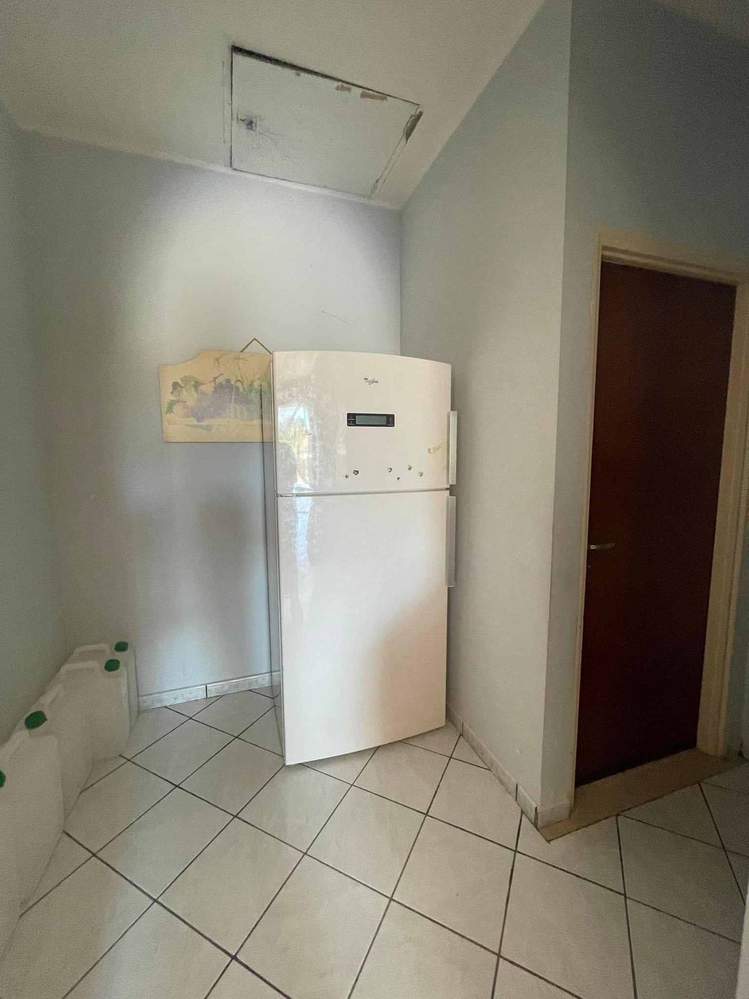 Piccola zona cucina con frigorifero bianco, pavimento piastrellato e una porta sulla destra.