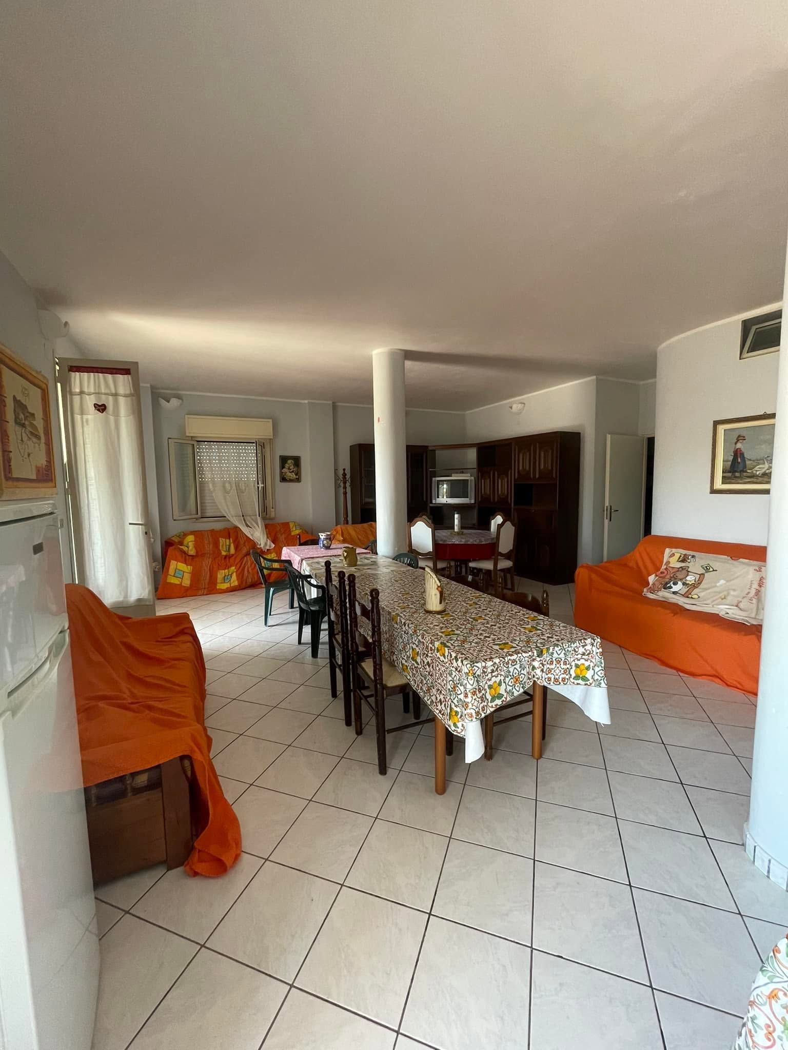 Luminoso soggiorno-sala da pranzo con tovaglia a fantasia, divani arancioni e pavimento piastrellato bianco.