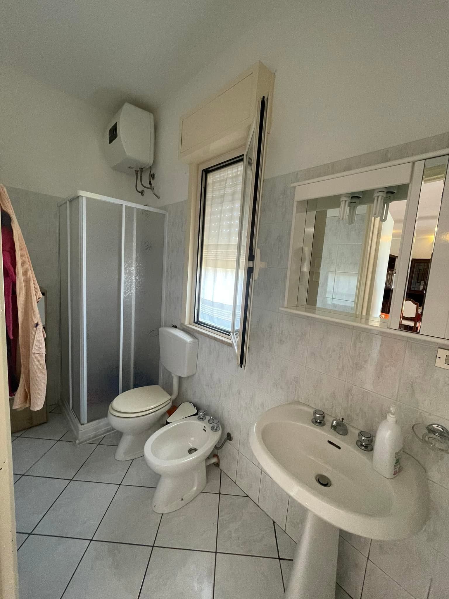 Bagno luminoso con doccia, WC, bidet, lavabo, specchio e pavimento piastrellato.