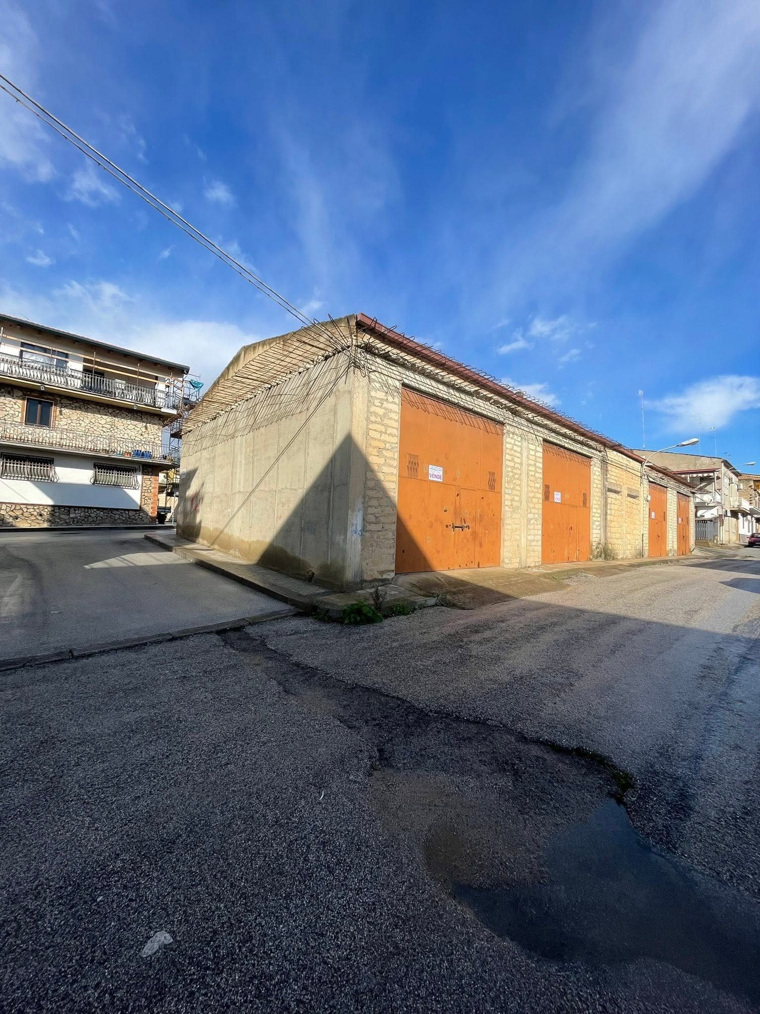 Vicolo soleggiato con portoni di garage arancioni accanto a edifici in pietra sotto un cielo azzurro