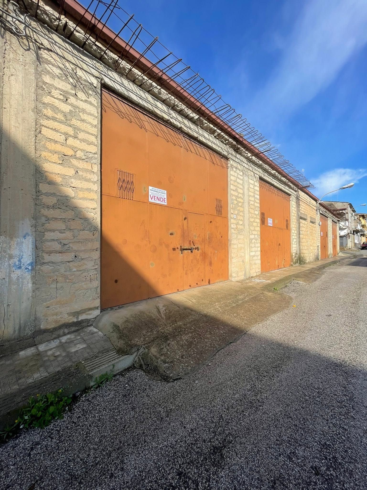 Una fila di porte da garage arancioni lungo una strada sterrata sotto un cielo azzurro