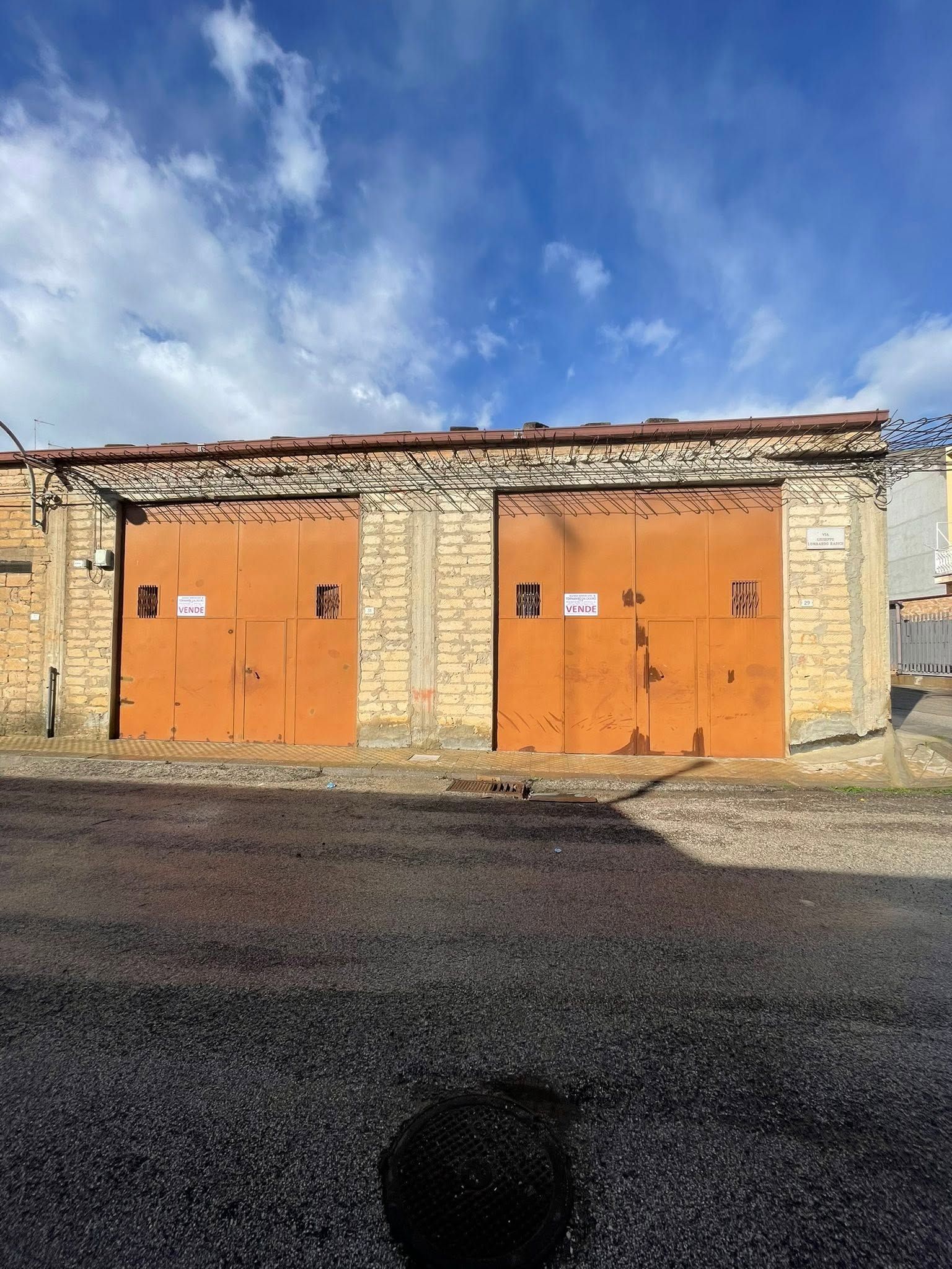 Garage rustico in pietra con due porte arancioni sotto un cielo azzurro nuvoloso.