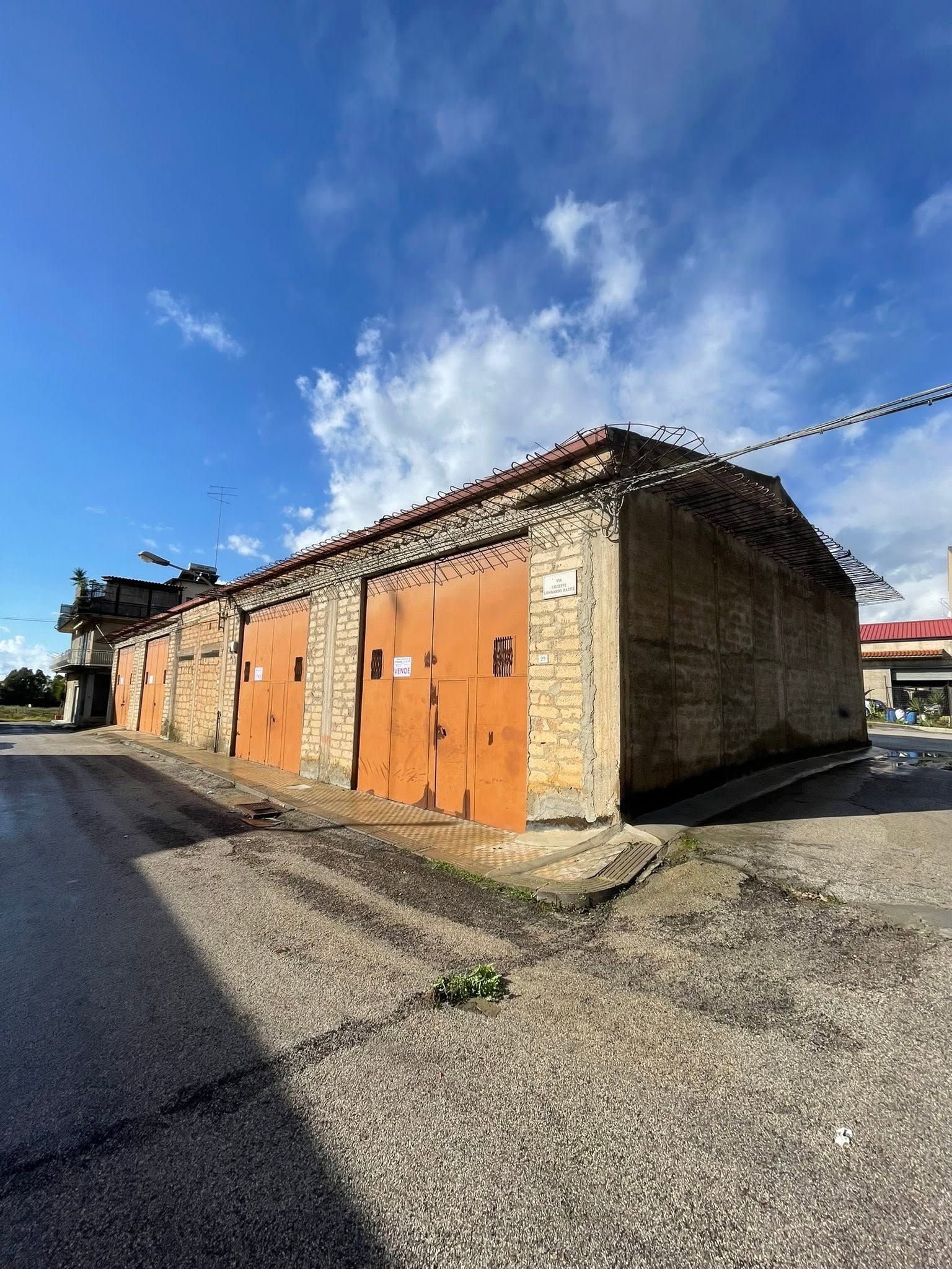 Vecchio garage in pietra con porte arancioni sotto un cielo azzurro su un piazzale ghiaioso