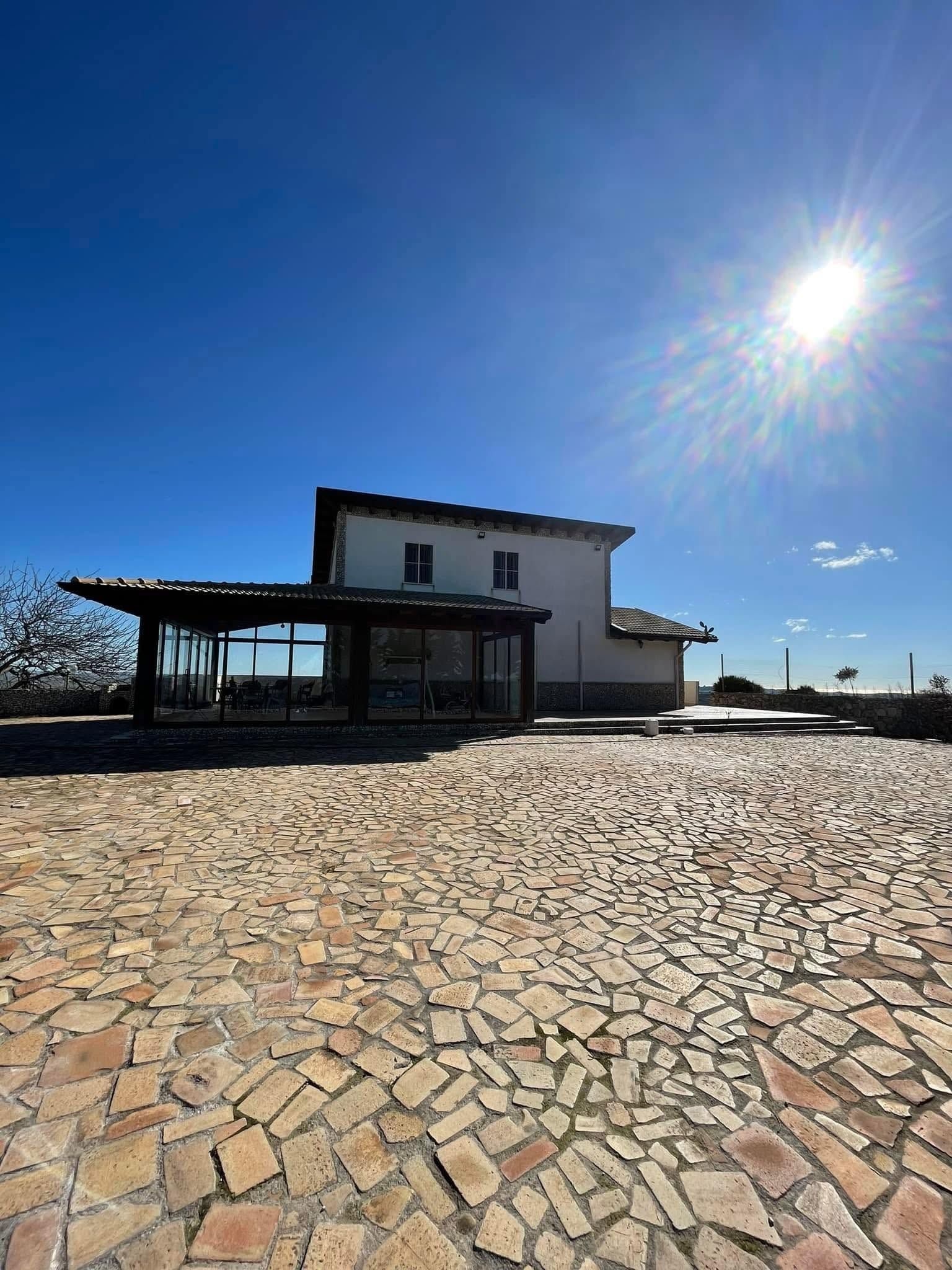 Casa rustica bianca con patio in pietra, baciata dal sole splendente e dal cielo azzurro limpido.
