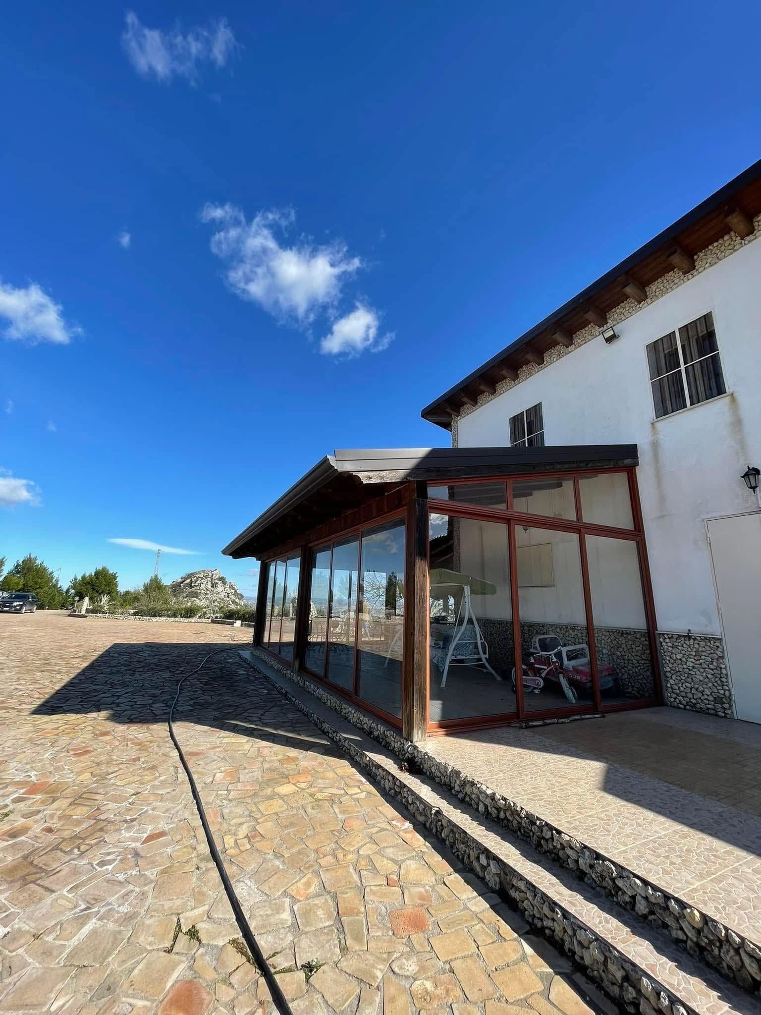 Edificio bianco con patio coperto e vialetto in pietra sotto un cielo azzurro brillante