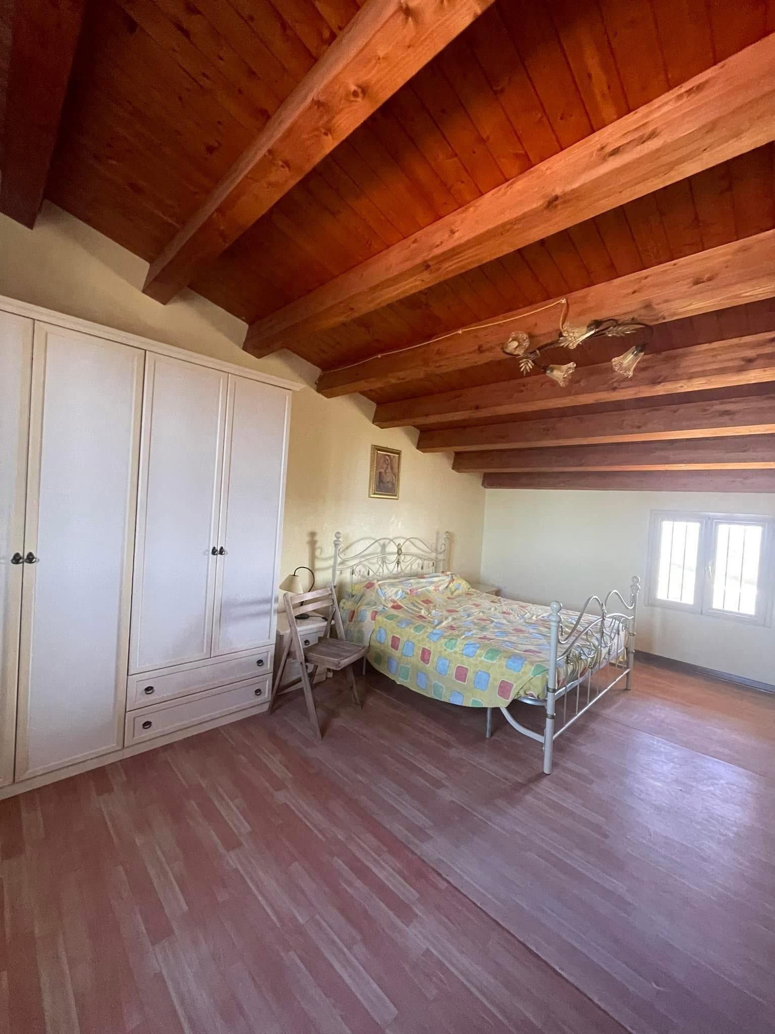 Camera da letto con travi in legno a vista, armadi bianchi e letto in metallo con biancheria da letto colorata.