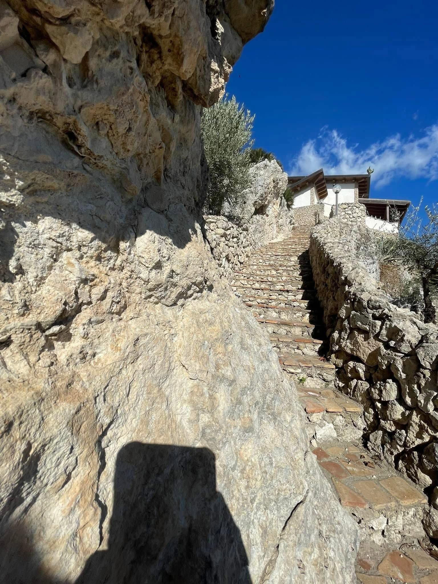Scalini di pietra scavati nella roccia conducono a un edificio bianco sotto un cielo azzurro.
