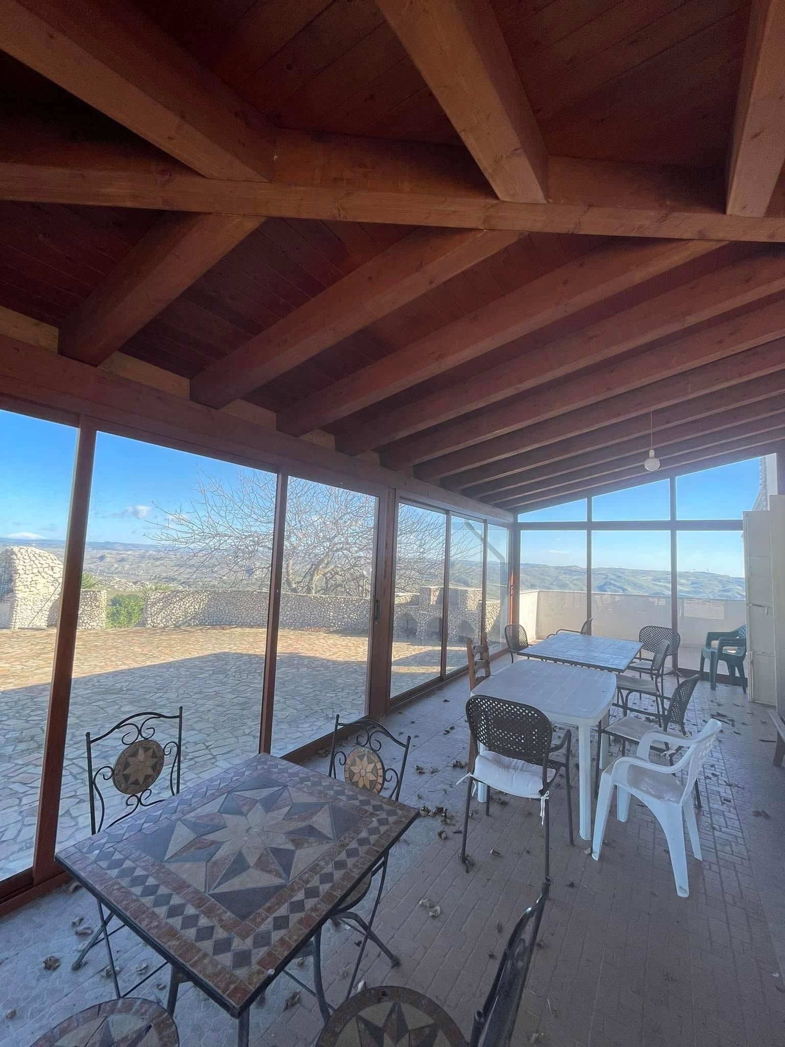 Patio coperto con travi in legno, pareti in vetro e mobili da giardino, affacciato su un paesaggio desertico.