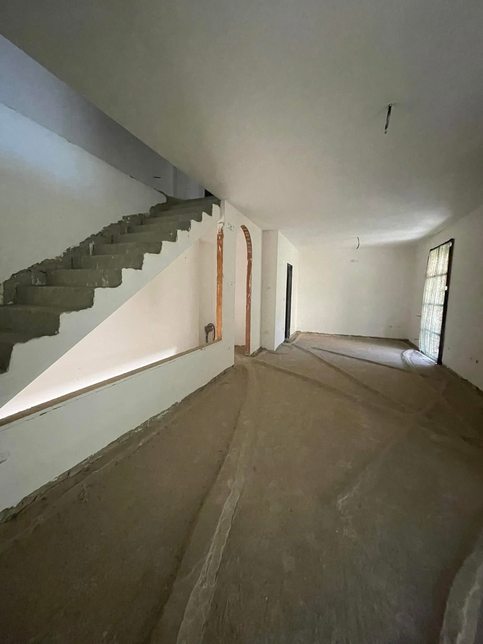 Stanza non finita con scala in cemento sulla sinistra, pareti spoglie e una porta in fondo.