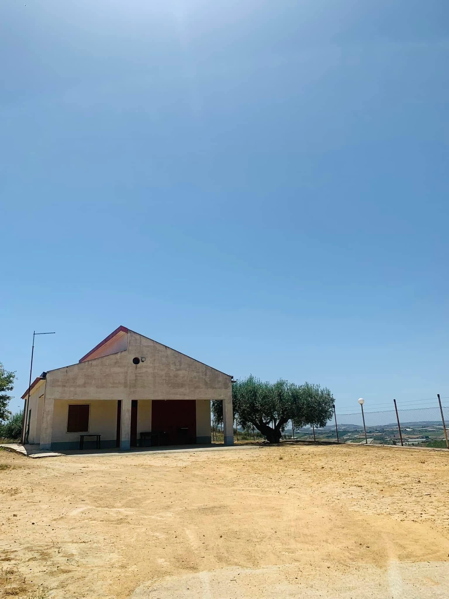 Un piccolo edificio fatiscente su un lotto sabbioso sotto un cielo azzurro e limpido, vicino all'acqua.
