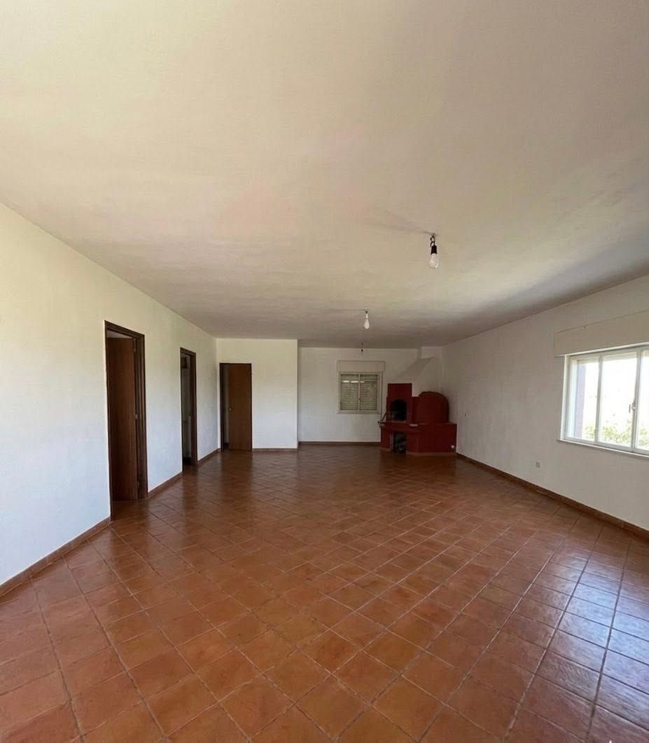 Soggiorno vuoto con pavimento piastrellato, pareti bianche, porte marroni e una sedia rossa vicino alla finestra in fondo.