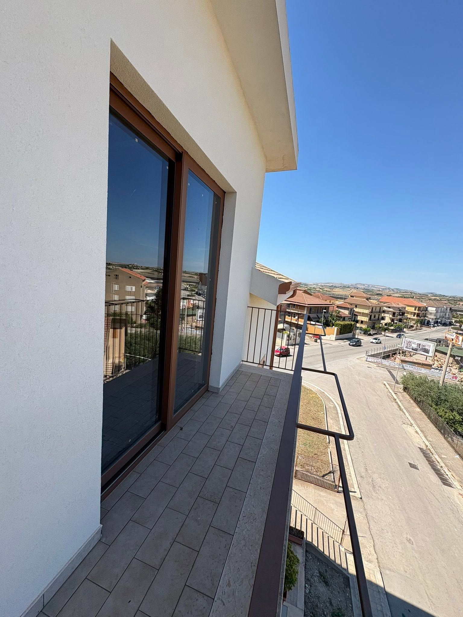 Balcone con porta in vetro nero affacciato su un quartiere collinare soleggiato e sulla strada