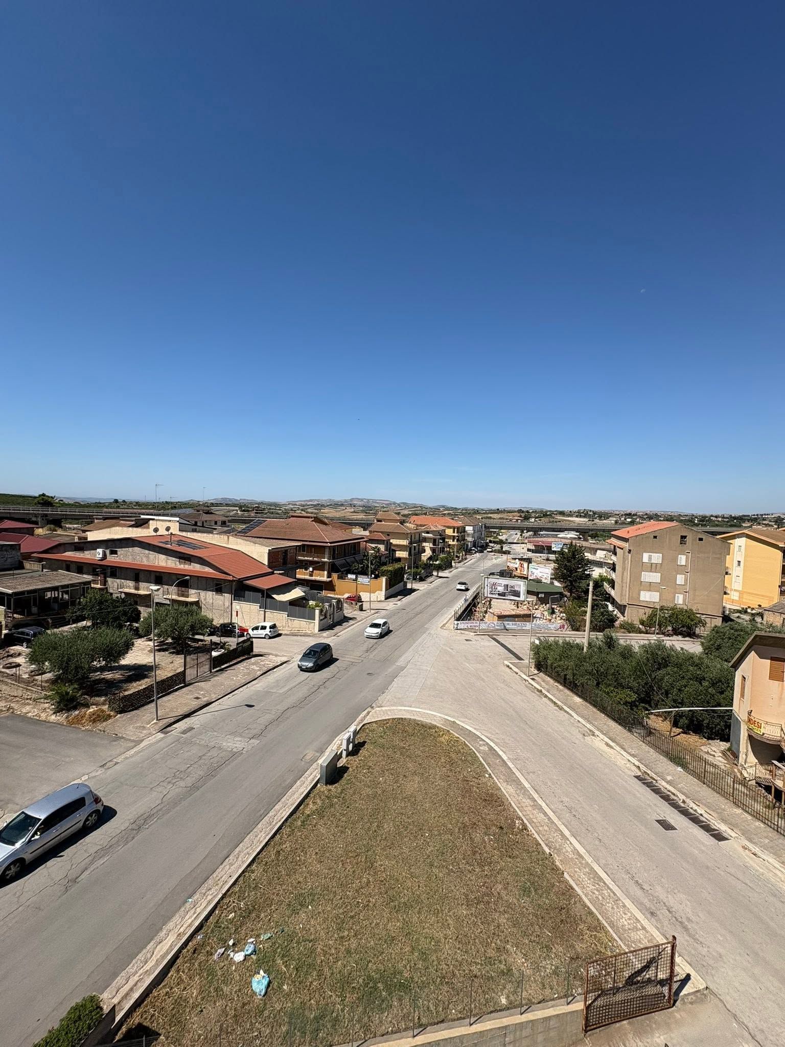 Ampia strada che attraversa un quartiere residenziale sotto un cielo azzurro e limpido, con case e auto su entrambi i lati.