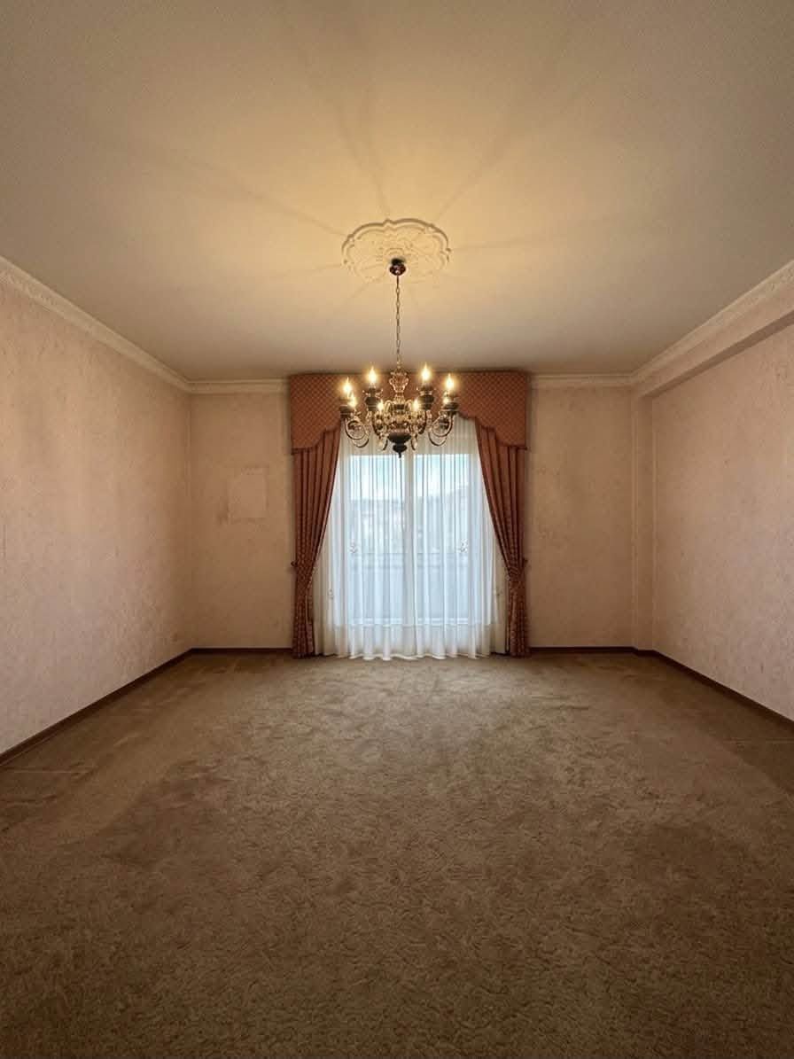 Stanza vuota con moquette, lampadario, tende e drappeggi trasparenti alle finestre.