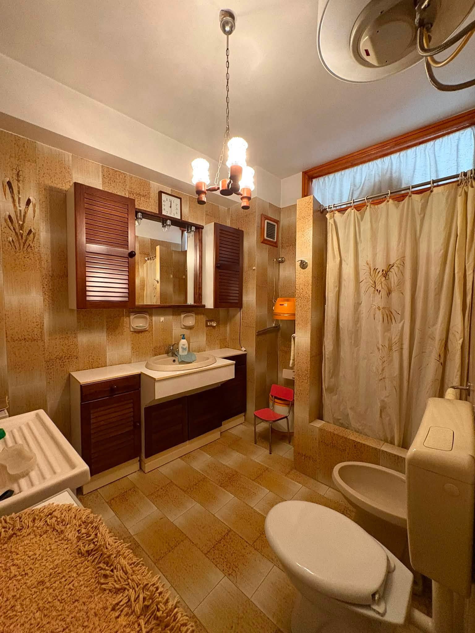 Bagno dai toni caldi con doppio lavabo, specchio, vasca da bagno con tenda e WC.