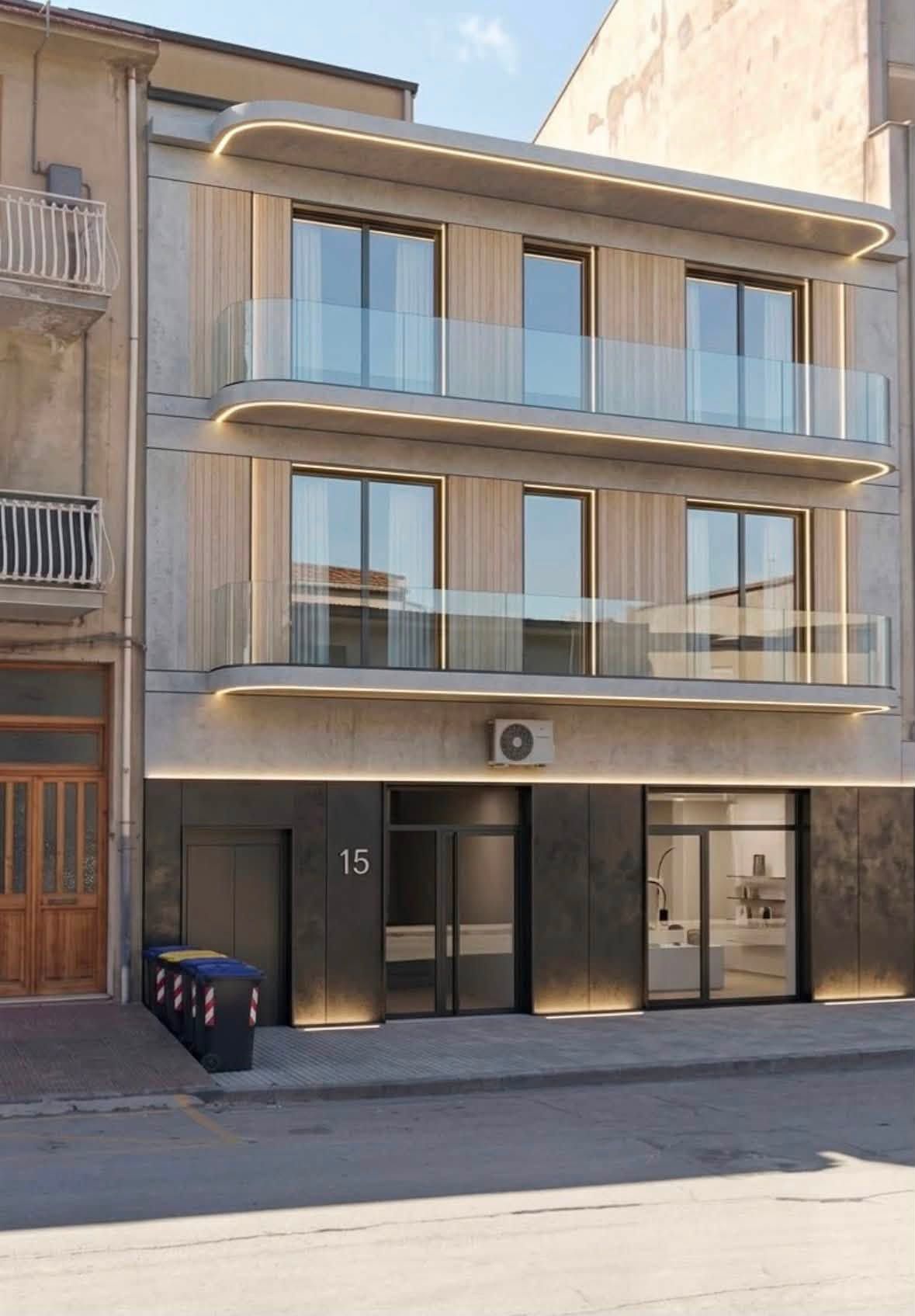 Moderno edificio residenziale di tre piani con facciata beige, balconi in vetro e ingresso a livello strada.