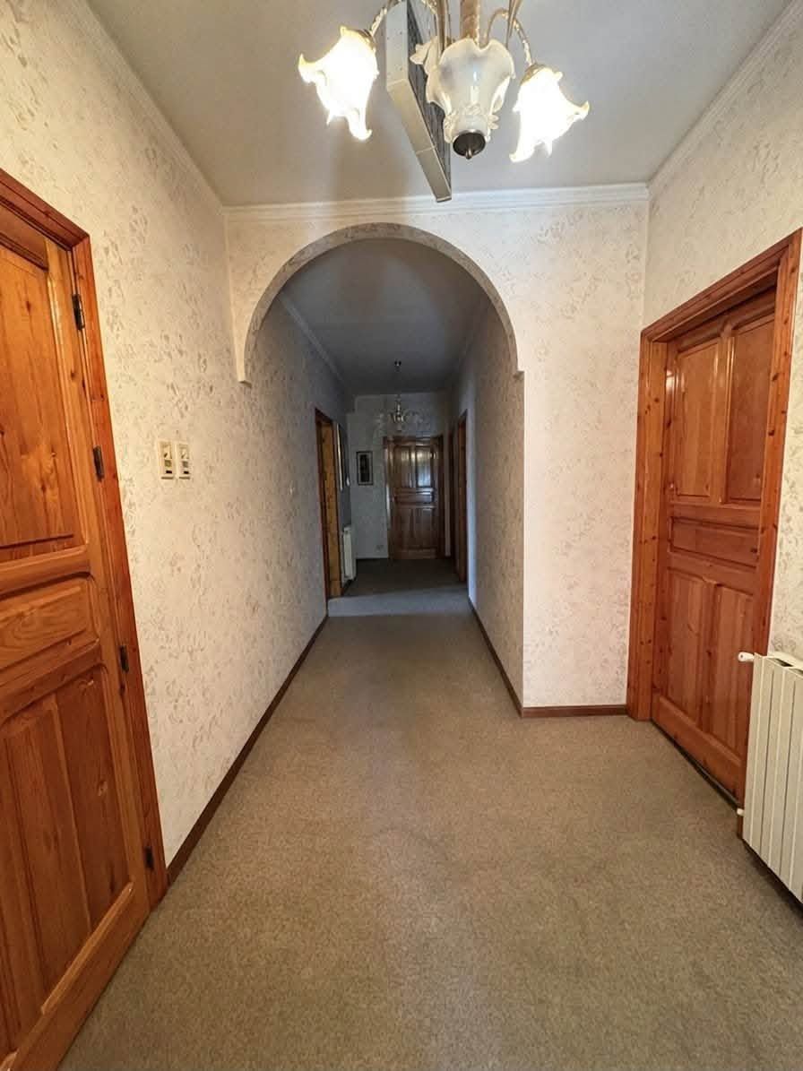 Stretto corridoio con porte in legno, moquette beige e un'apertura ad arco che conduce a un corridoio meno illuminato.