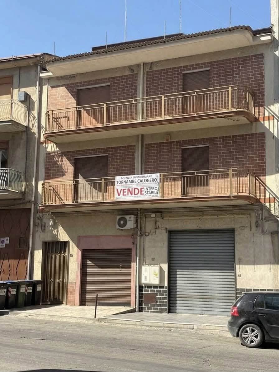 Palazzo di mattoni con appartamenti, balconi e serrande di negozi chiuse, uno dei quali con l'insegna 