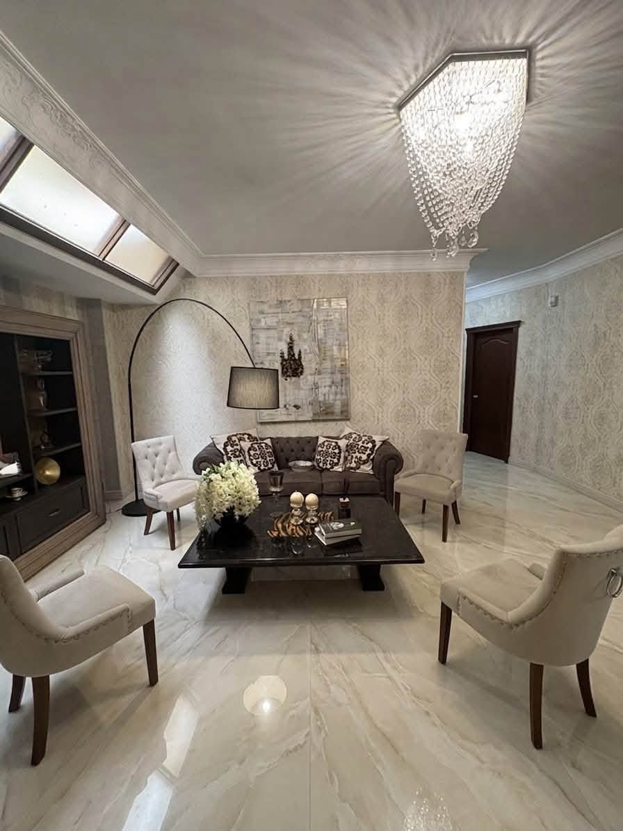 Elegante soggiorno beige con lampadario, tavolino da caffè scuro, divano e lampada da terra ad arco.